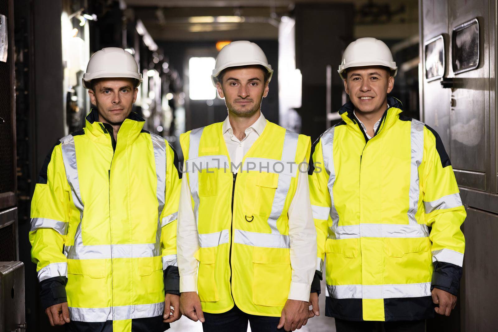 Portrait of group of professional telecommunication industry engineers smiles and looks at the camera . Workers wearing safety uniform and hard hat on unfocused background.