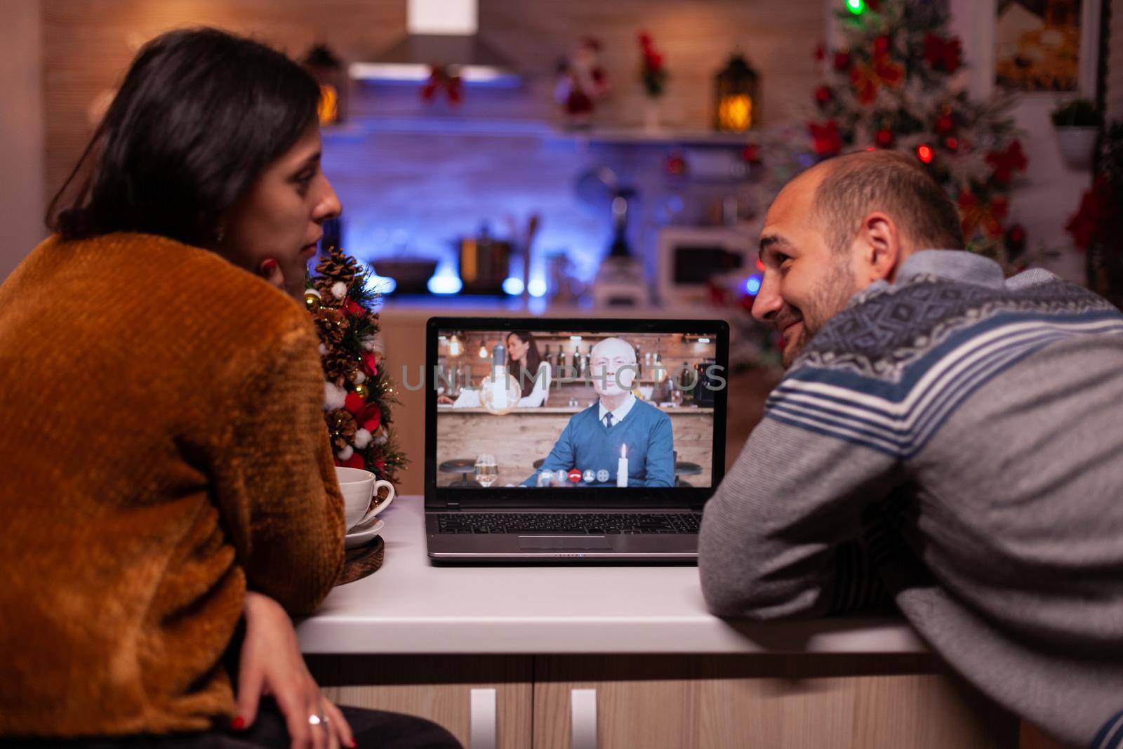 Happy family discussing with remote grandparent during online videocall conference celebrating christmas holiday together in xmas decorated kitchen. Joyful couple enjoying winter season