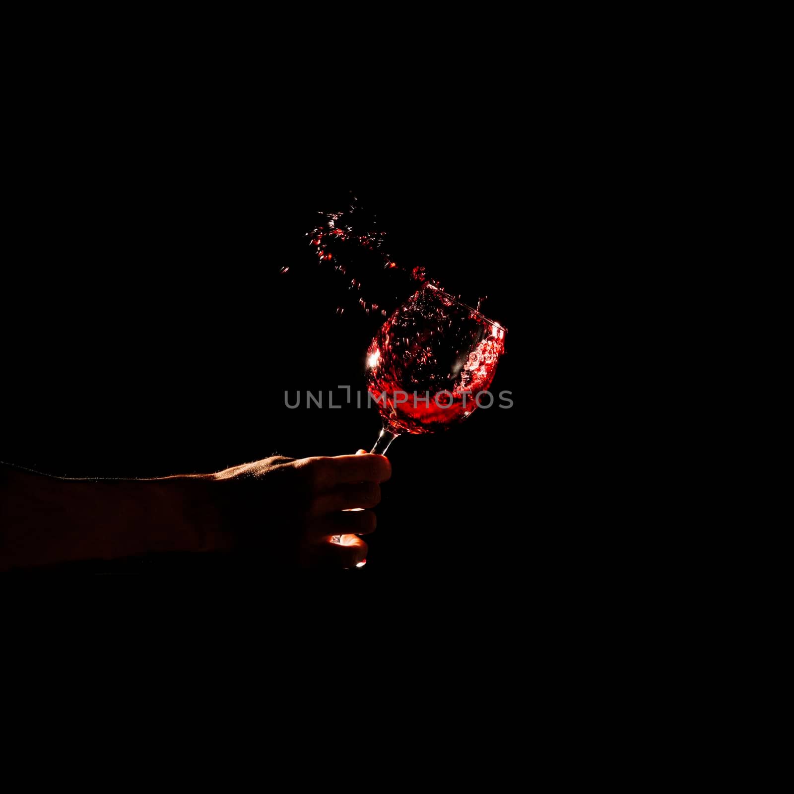 person s hand holding glass red wine splashing out glass. High resolution photo