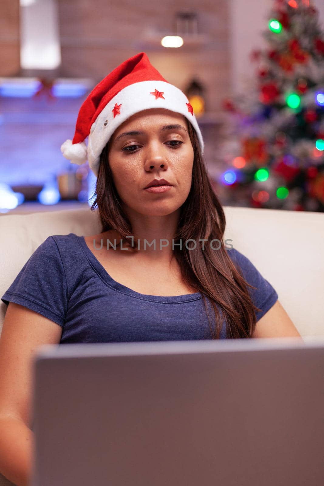 Girl reading business email on laptop computer working during christmastime sitting on couch in xmas decorated kitchen. Woman celebrating winter holiday enjoying christmas season