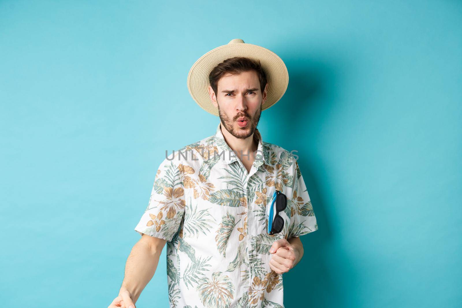 Happy tourist in hawaiian shirt and summer hat dancing, having fun on vacation, standing on blue background by Benzoix