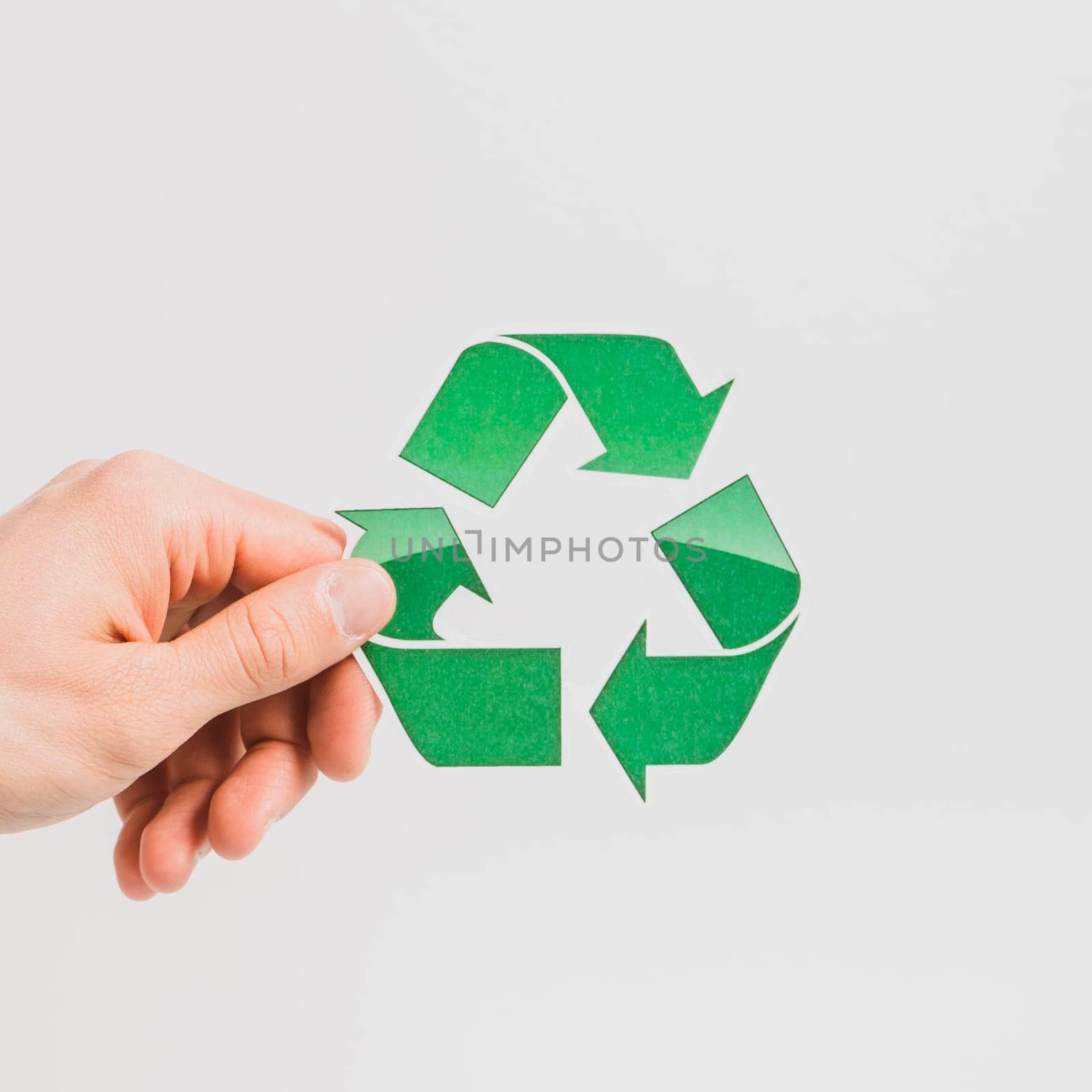 person s hand holding green recycle symbol white backdrop. High resolution photo
