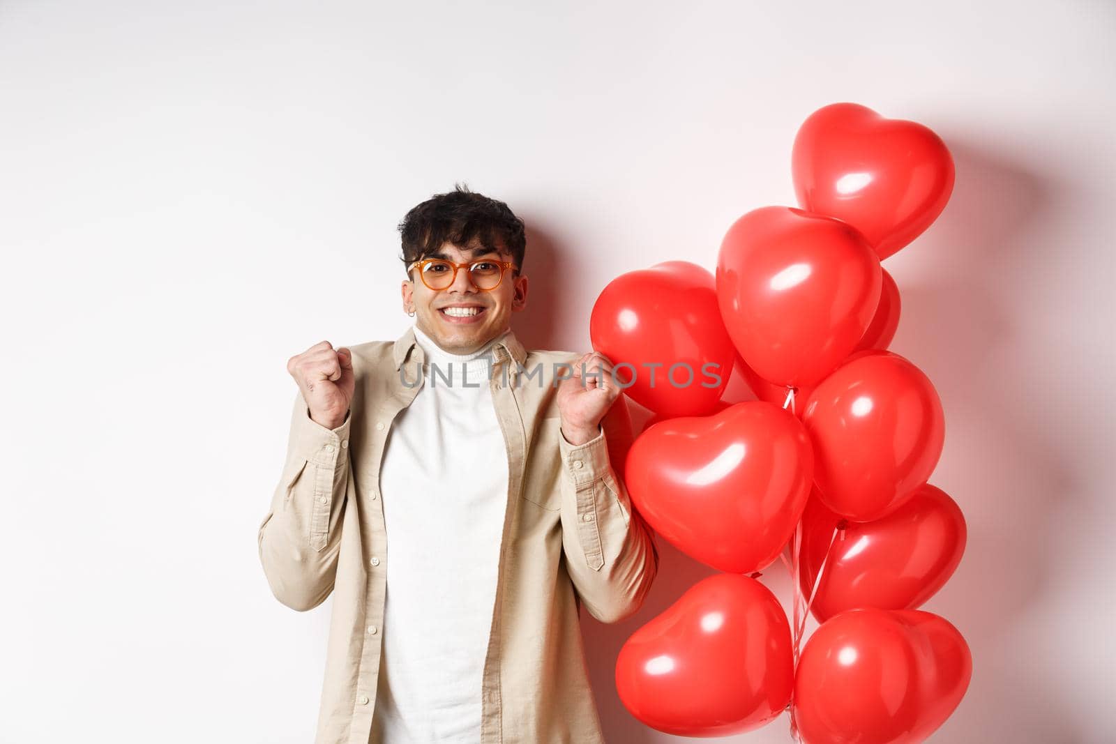 Valentines day. Excited smiling man eager to go on date, celebrating with lover, standing near red hears balloons, white background by Benzoix