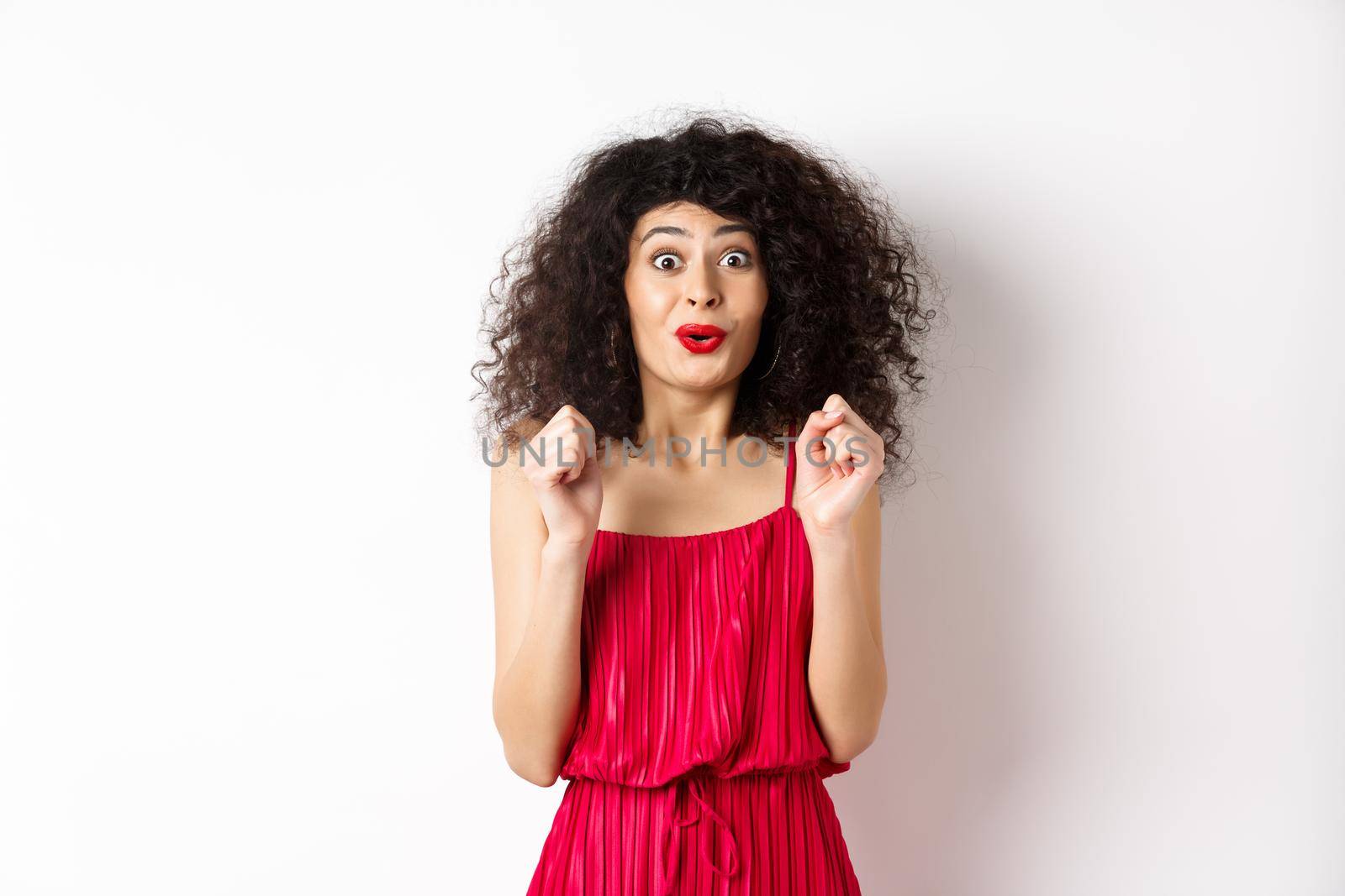 Excited smiling woman eager to try something, jumping from amusement and smiling, wearing red dress, standing on white background by Benzoix