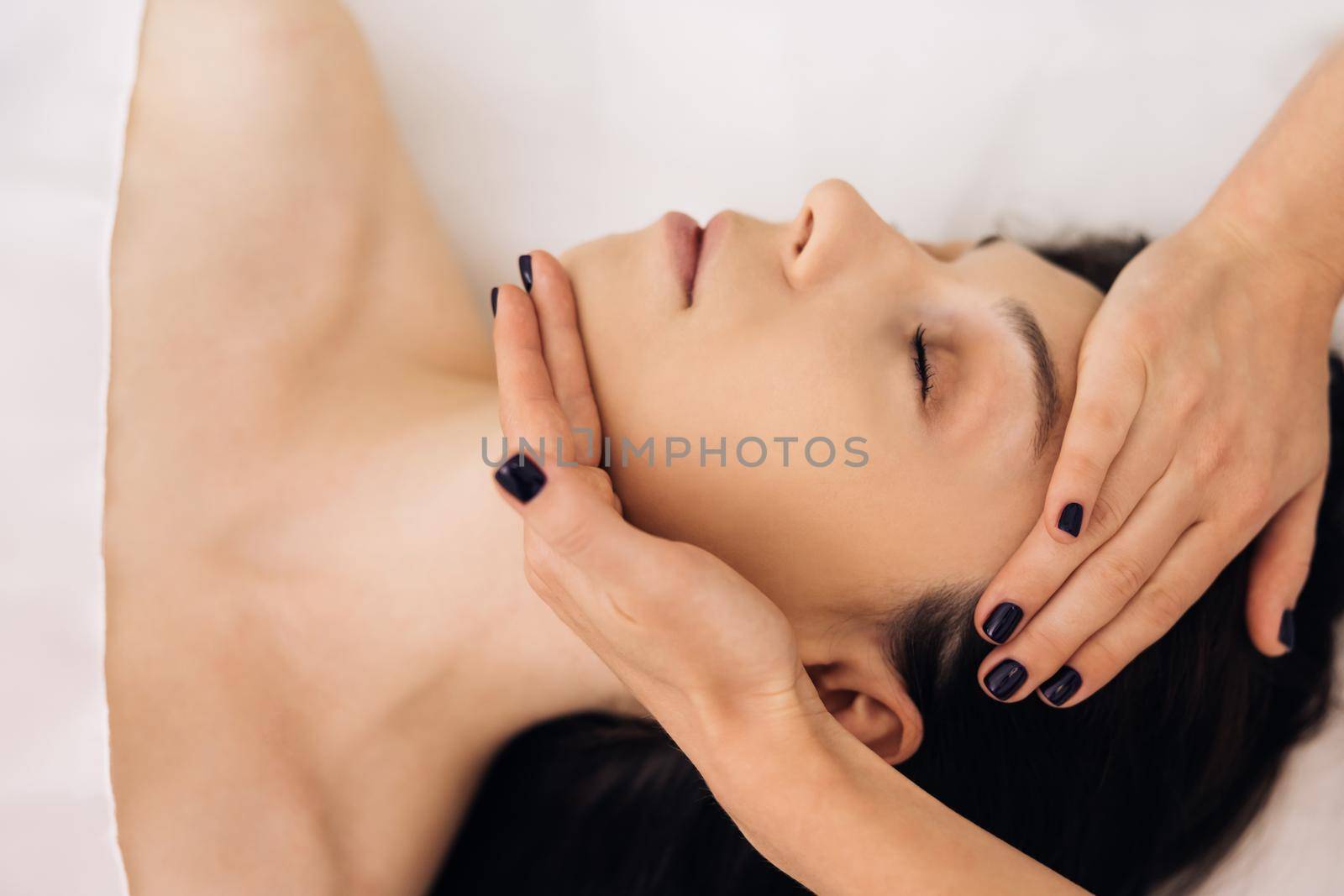 Young Caucasian woman lying on spa bed get facial massage treatment with aroma essential oil skincare from massage therapist at beauty salon. Wellness health care body massage spa concept.