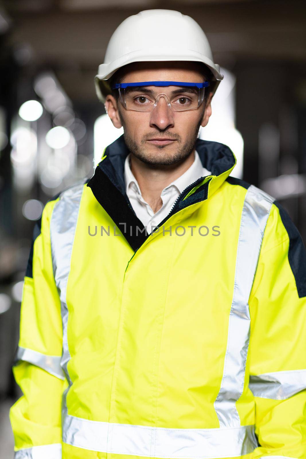Caucasian Industrial Specialist Standing in a Metal Construction Manufacture. Professional Heavy Industry Engineer Worker Wearing Uniform, Glasses and Hard Hat in a Steel Factory Looks at Camera by uflypro