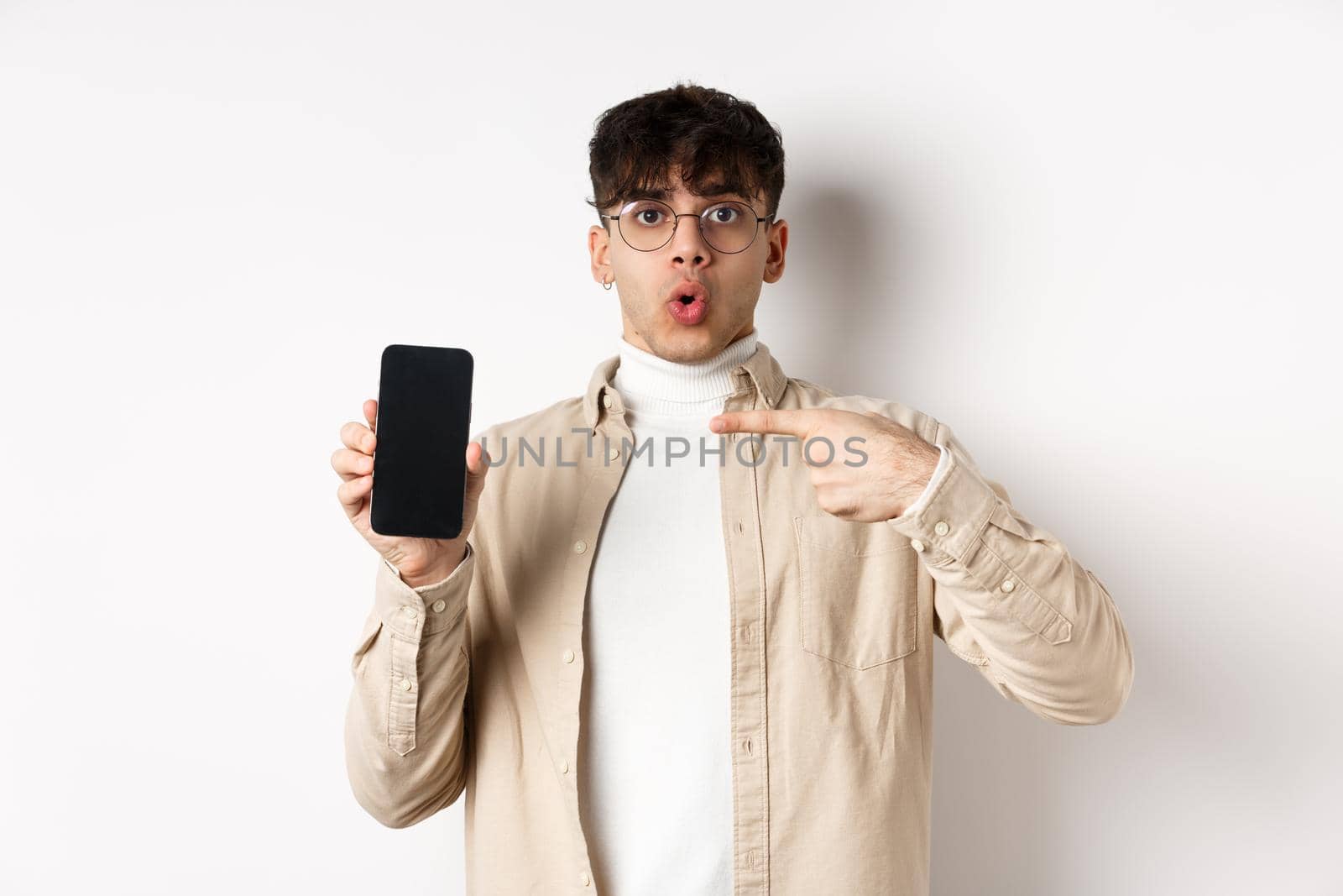 E-commerce concept. Portrait of young man pointing at mobile phone screen, showing advertisement online, standing on white background by Benzoix