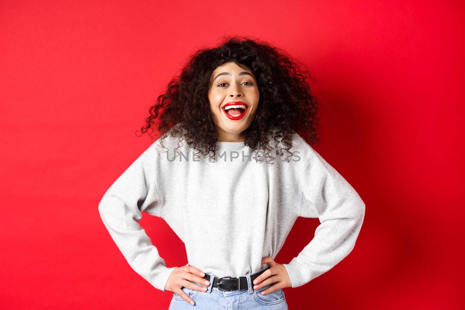 Excited positive woman laughing and smiling, feeling upbeat, looking at funny promo, standing on red background.