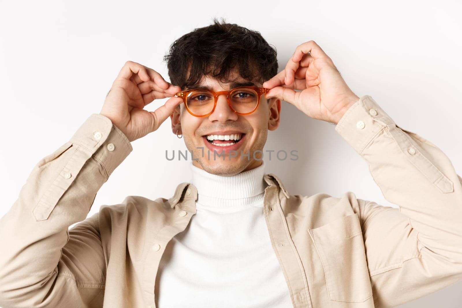 Close-up of stylish hipster guy trying eyewear at optician store, put on glasses and smiling, standing on white background by Benzoix