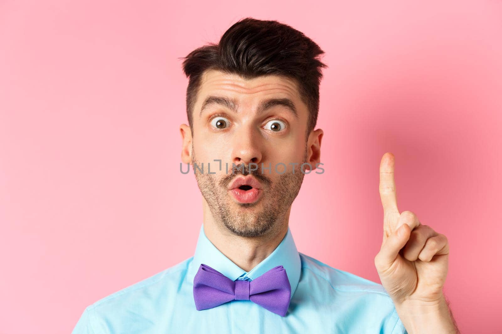 Close-up of excited funny guy with moustache and bow-tie, pitching an idea, raising finger to say suggestion, have plan, standing over pink background by Benzoix