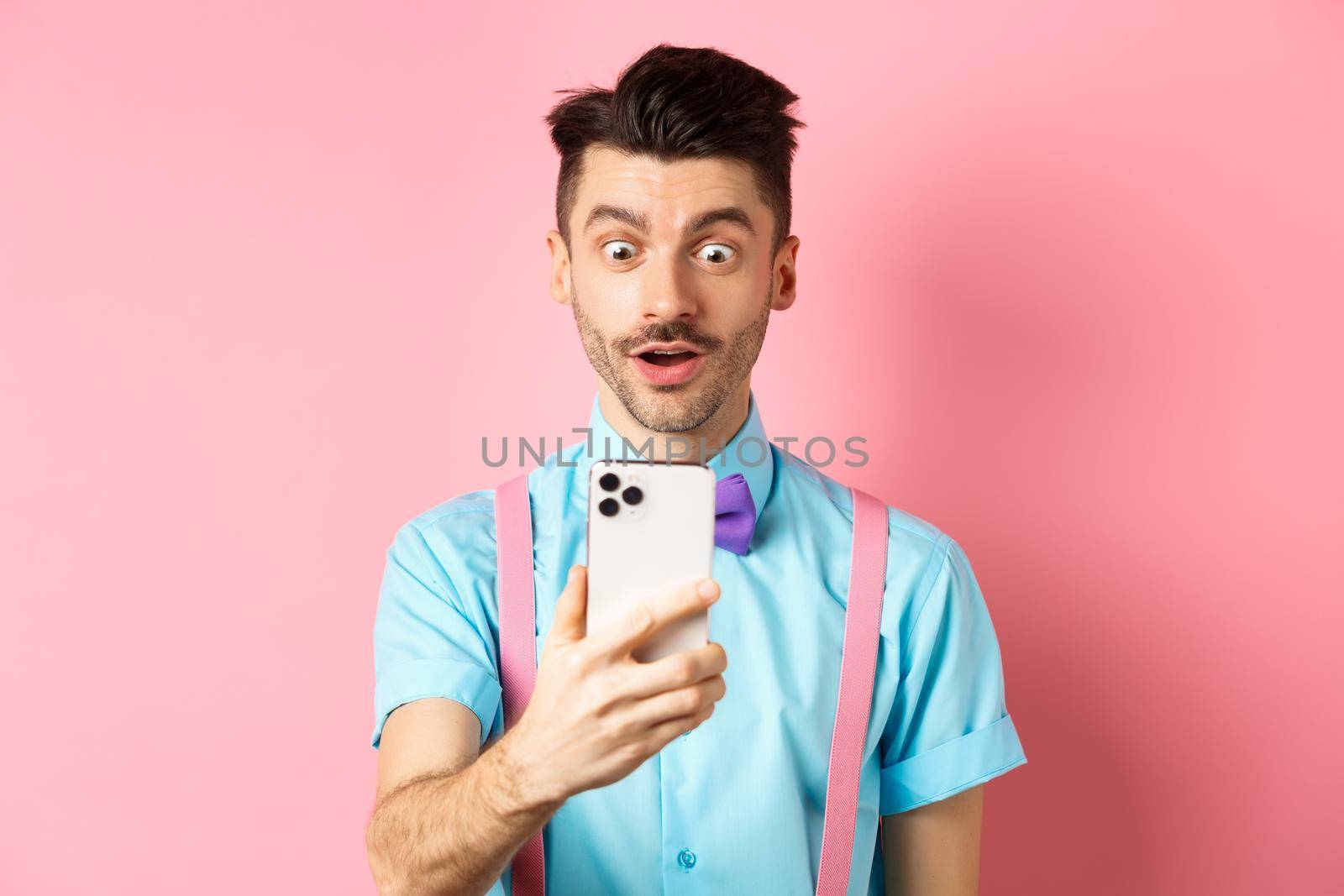 Impressed man reading mobile screen with amazed face, seeing online promo offer, standing over pink background by Benzoix