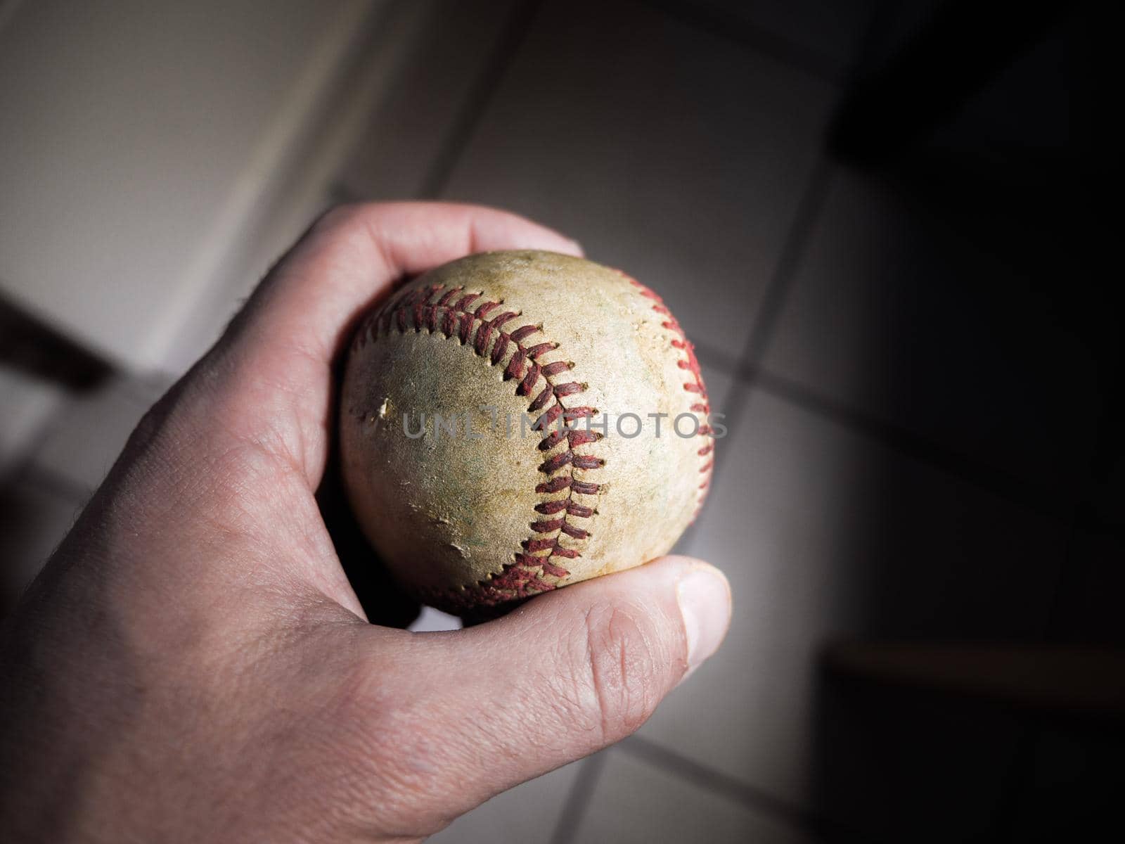 Close up sports background image of a male hand holding an old used weathered leather baseball between his thumb and fore finger showing intricate detailing and red laces.