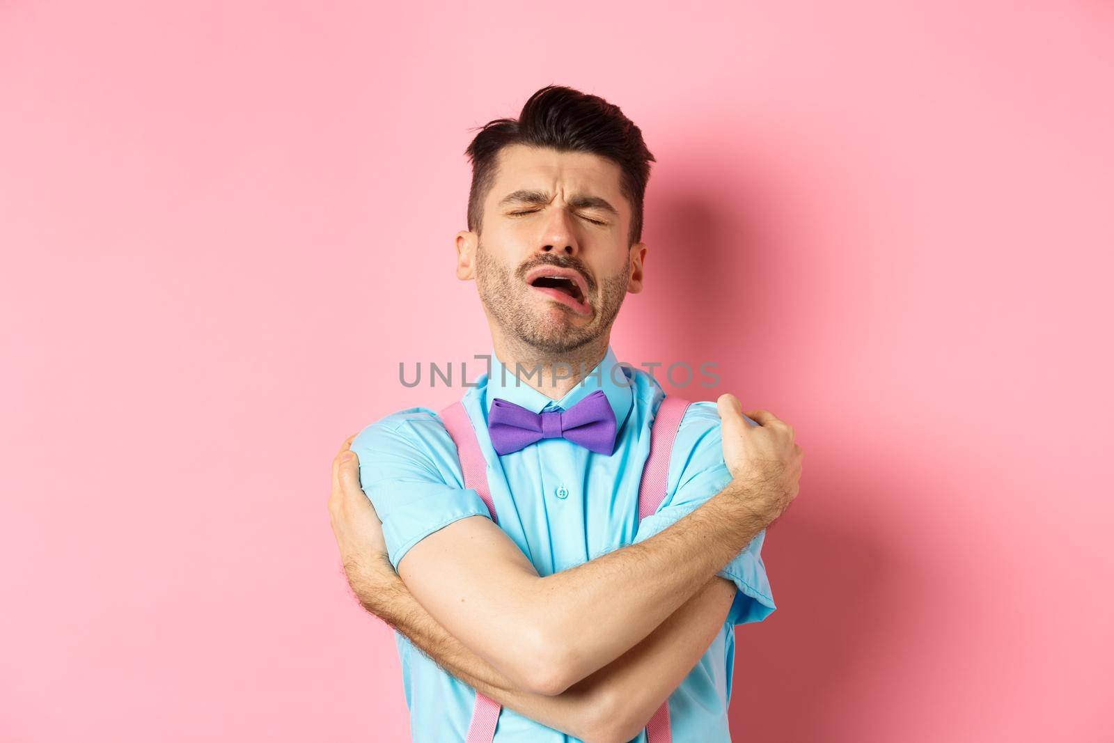 Crying guy hugging himself, feeling sad and lonely, standing unhappy on pink background by Benzoix