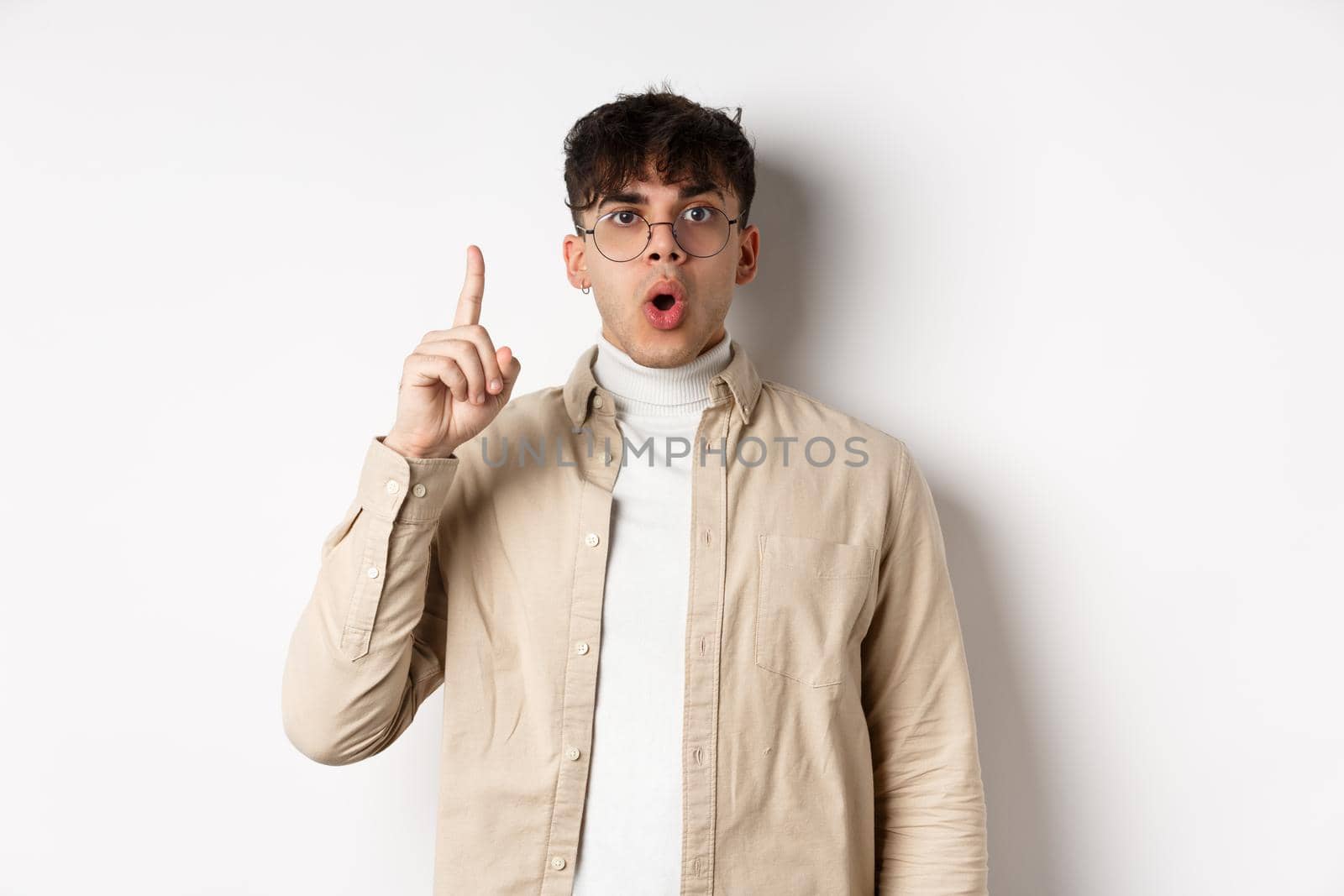 Portrait of young man student pitching an idea, raising finger up and say suggestion, have a plan, standing on white background in glasses and casual clothes.
