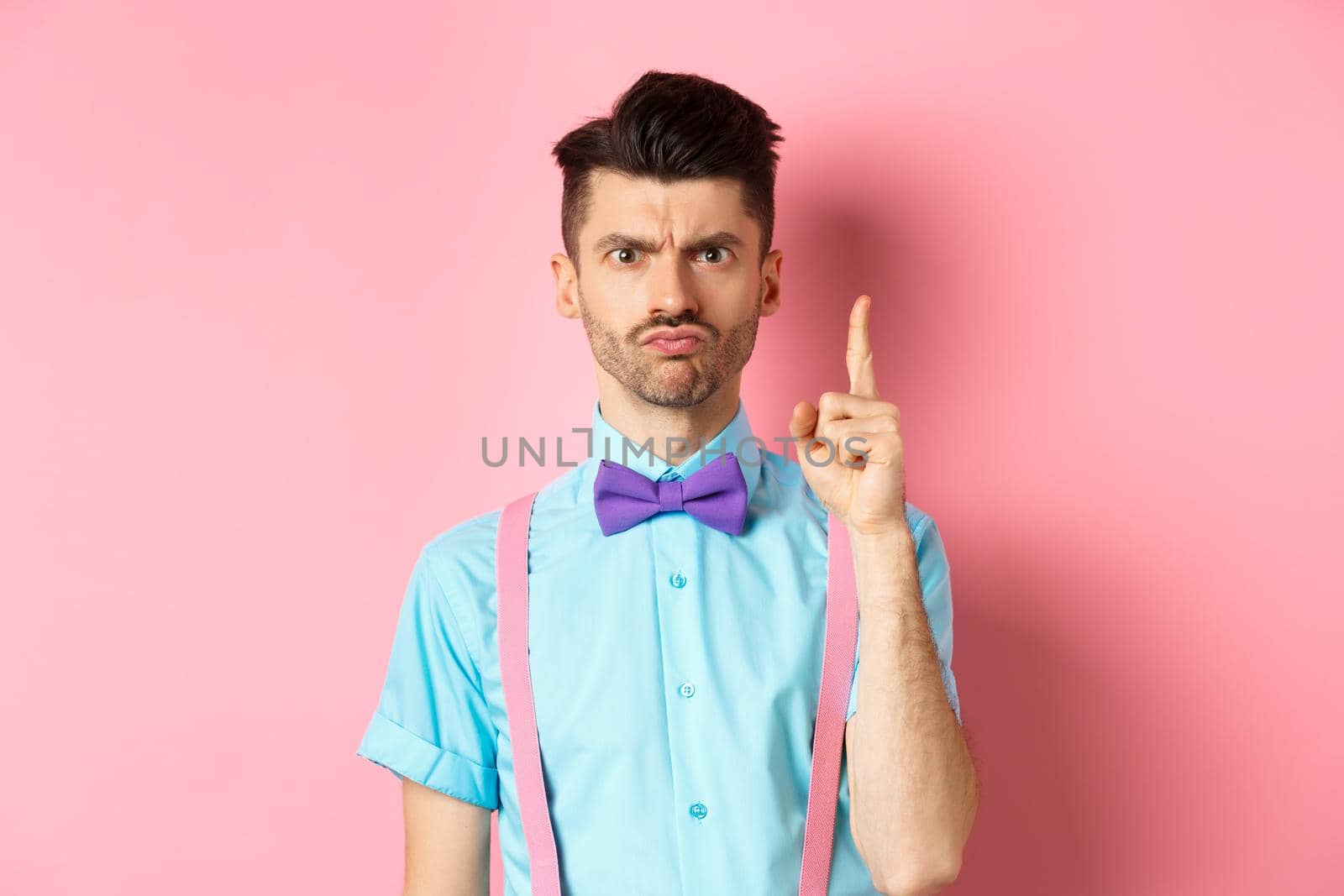 Angry male teacher shaking finger and scolding someone who misbehave, frowning grumpy, and teaching lesson, standing over pink background.