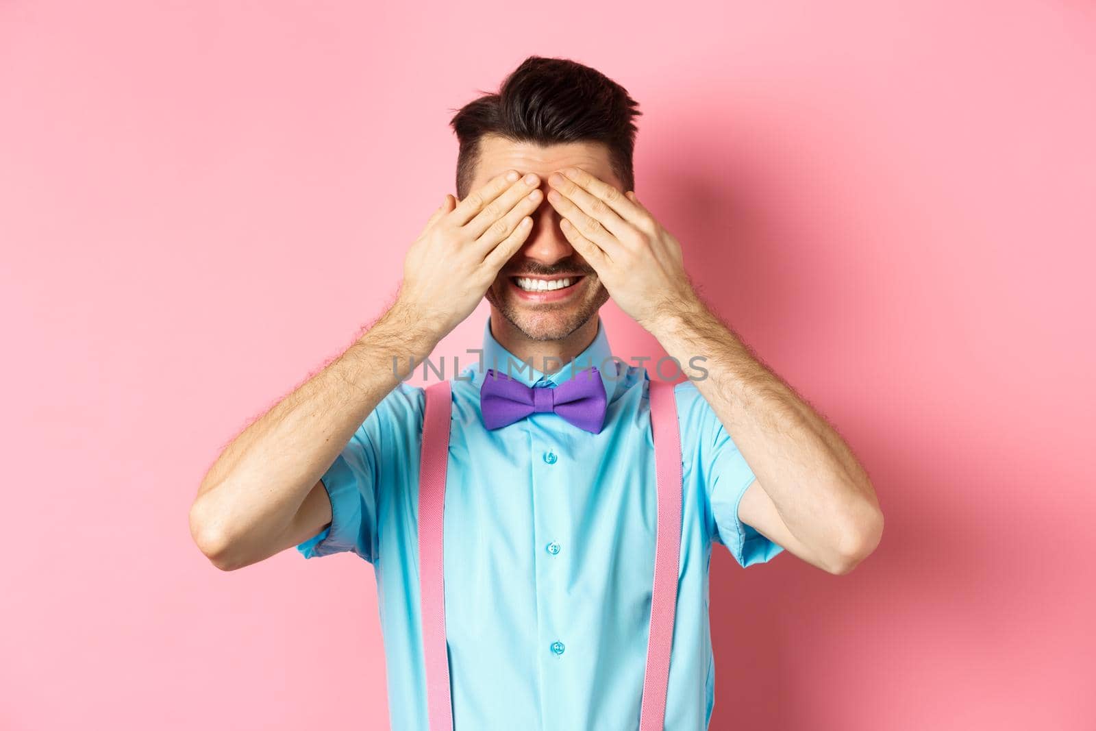 Image of smiling handsome guy waiting for surprise with closed eyes, standing in fancy outfit on pink background by Benzoix
