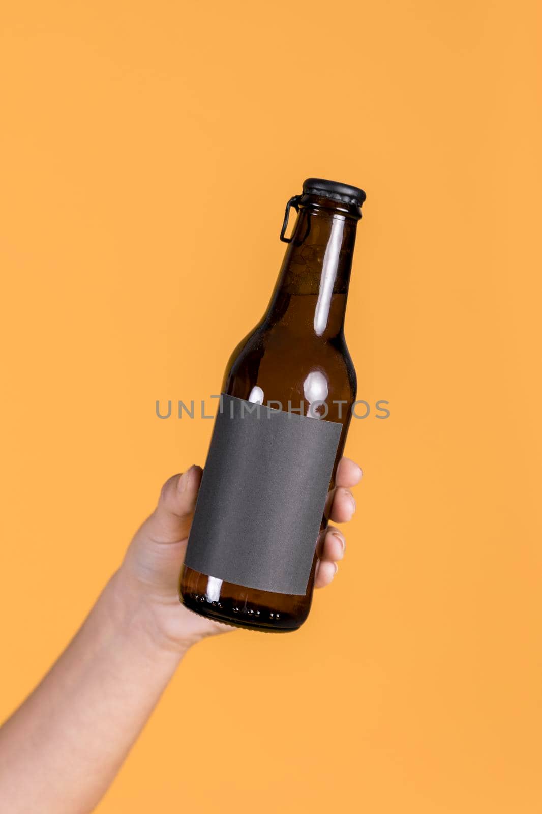 human hand holding brown beer bottle against yellow wall backdrop. High resolution photo