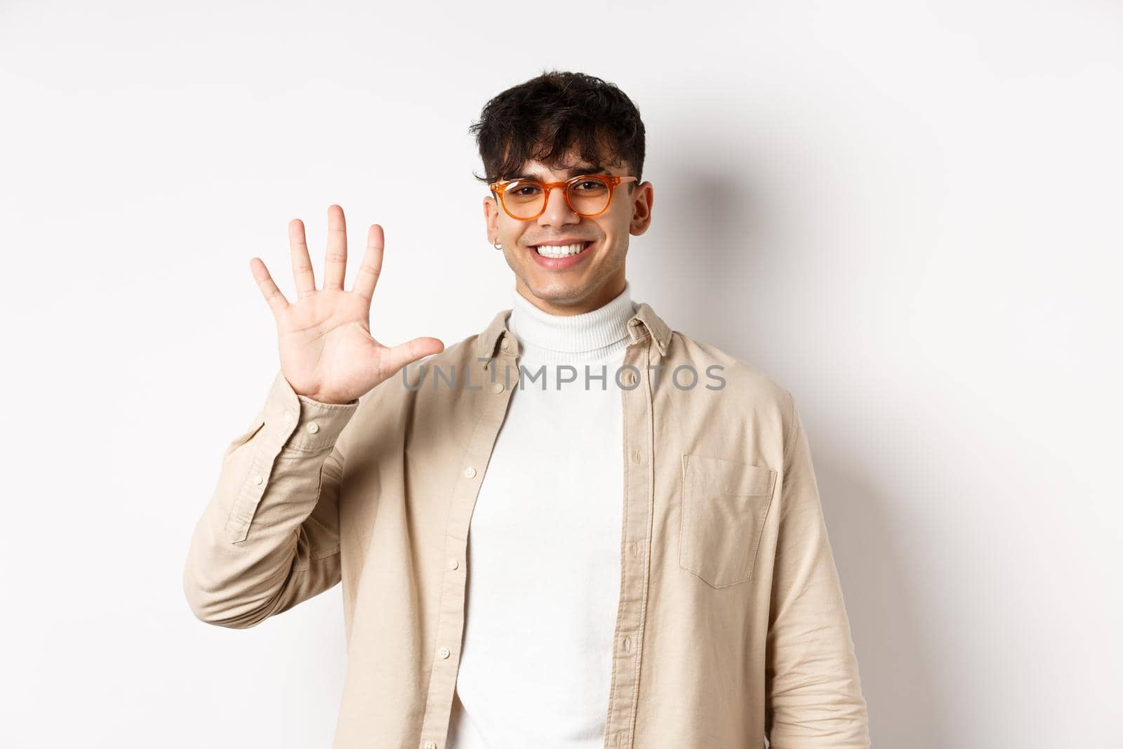 Modern guy in glasses and stylish outfit, showing five fingers number and smiling, making order, standing on white background by Benzoix