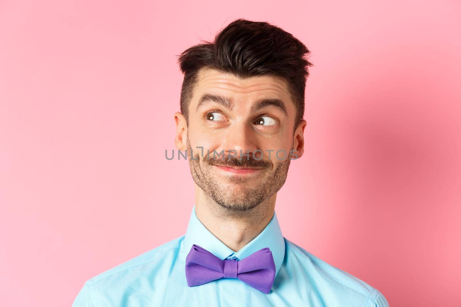 Close-up of handsome smiling guy with moustache, looking left at logo with pleased face, standing on pink background by Benzoix