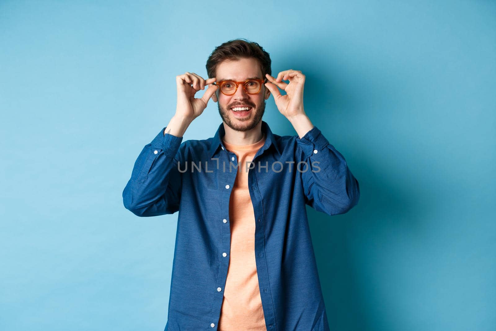 Happy caucasian man trying new glasses and smiling, standing on blue background.