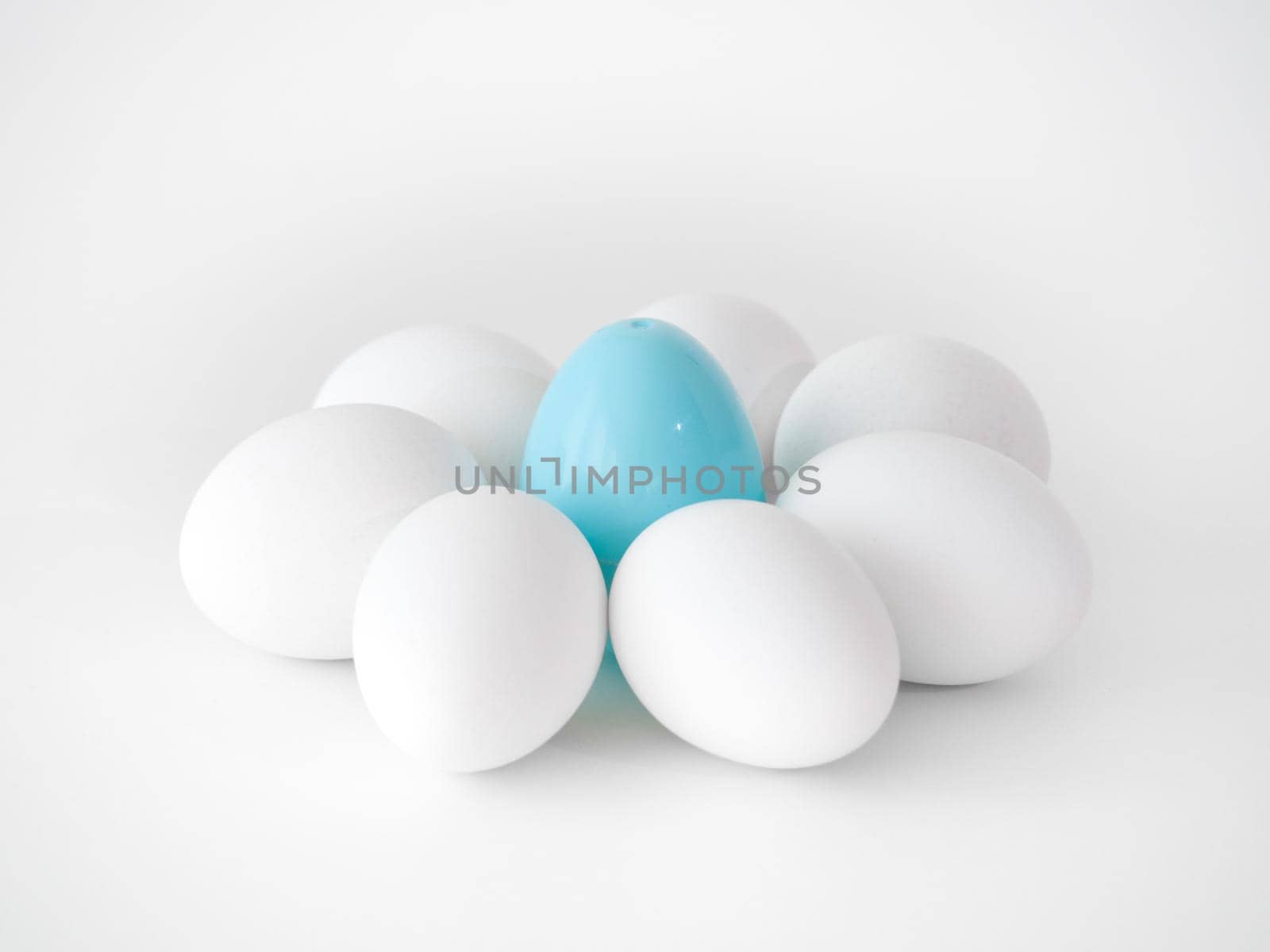 Photograph of a cute flower shape created from the arrangement of white chicken eggs as petals and a blue plastic Easter egg at the center making a great holiday background image.