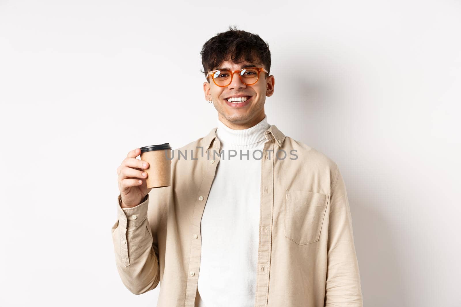 Real people. Happy young man drinking coffee from paper cup, order takeaway at favourite cafe, smiling and looking pleased at camera, white background by Benzoix