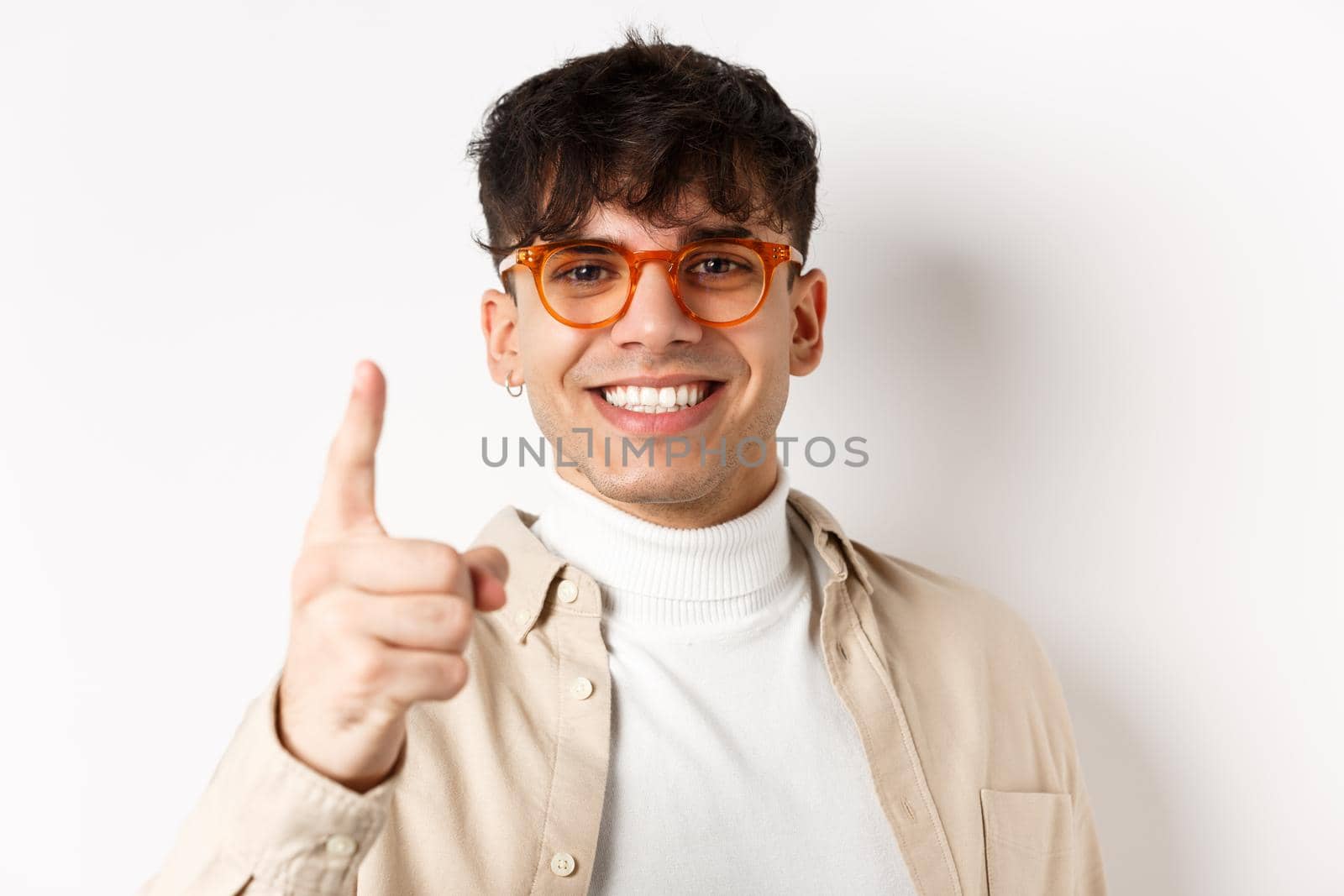 Close-up of lucky handsome man in glasses, smiling and pointing finger at camera, praising something good, standing on white background.