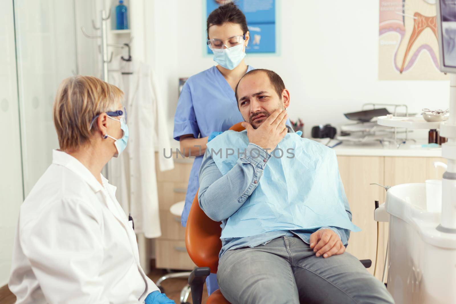 Stomatologist doctor talking to man patient with toothache sitting on dental chair preparing for medical examination. Dentists team working in stomatology hospital clinic office