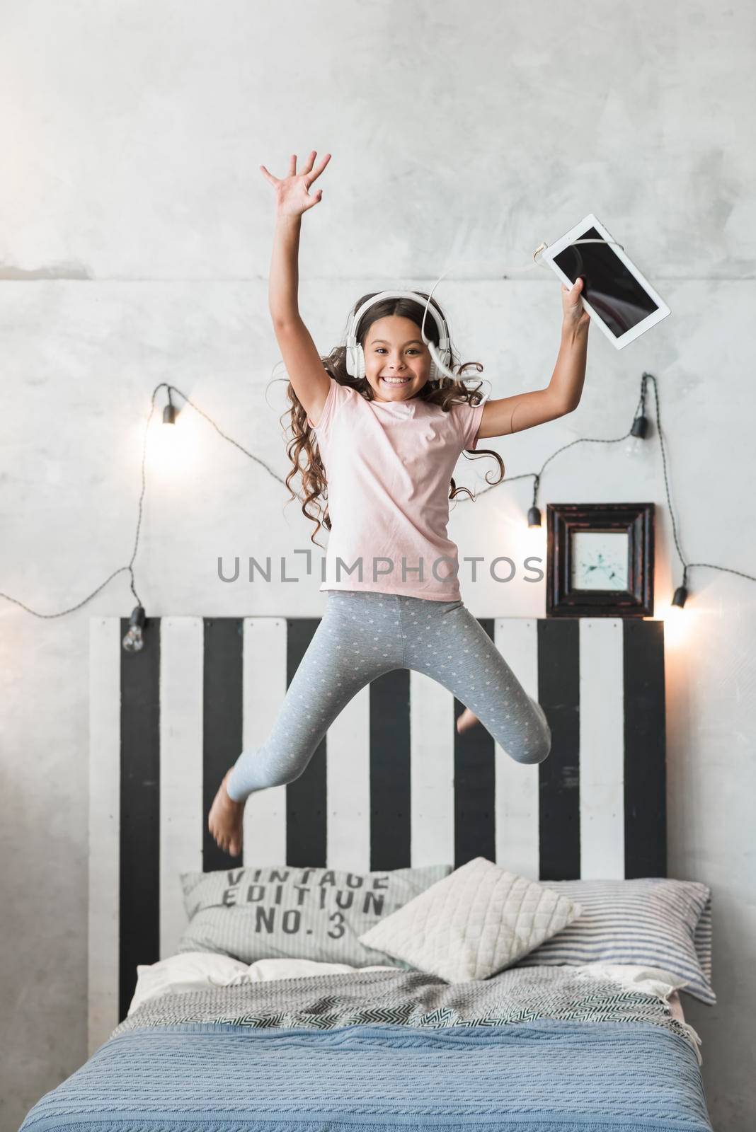 excited smiling girl jumping bed with headphone digital tablet. High resolution photo