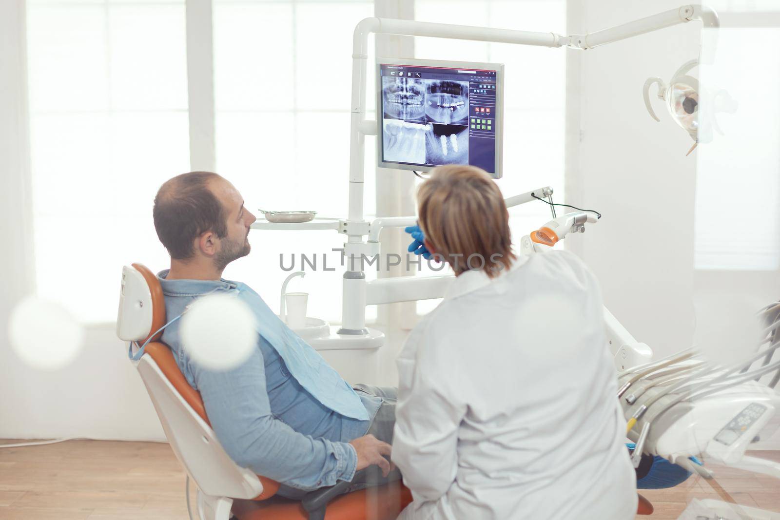 Stomatologist discussing with patient sitting in stomatological chair by DCStudio
