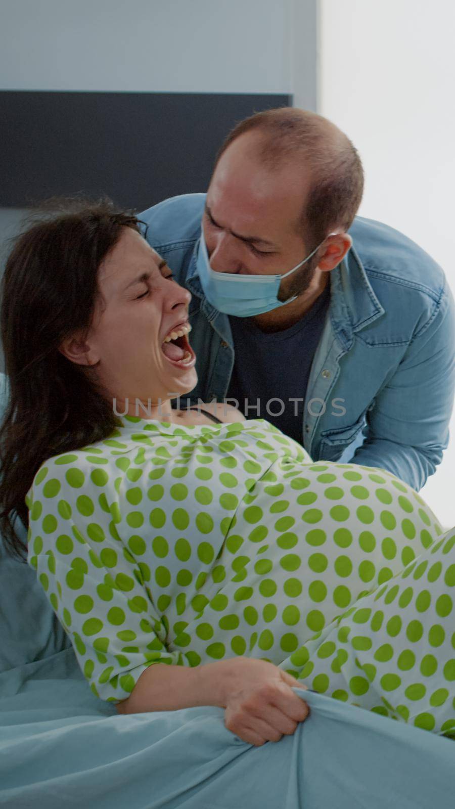 Pregnant patient in painful childbirth pushing for baby laying in hospital ward bed. Multi ethnic nurse and maternity doctor giving assistance to caucasian woman for child delivery