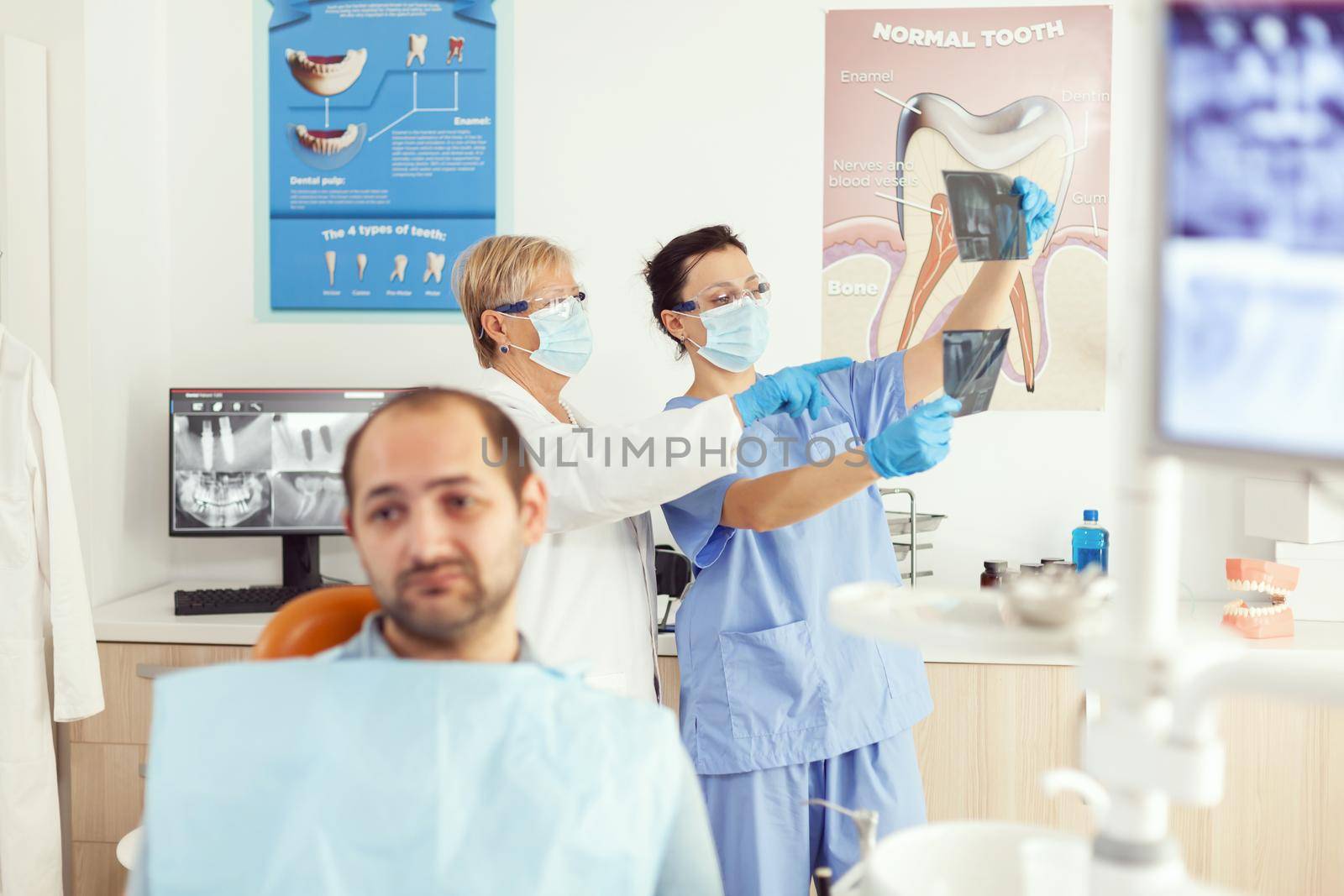 Sick man patient waiting for teeth examination sitting on dental chair in stomatology clinic room. Stomatologist doctor and medical nurse preparing for orthodontic surgery while examining radiography