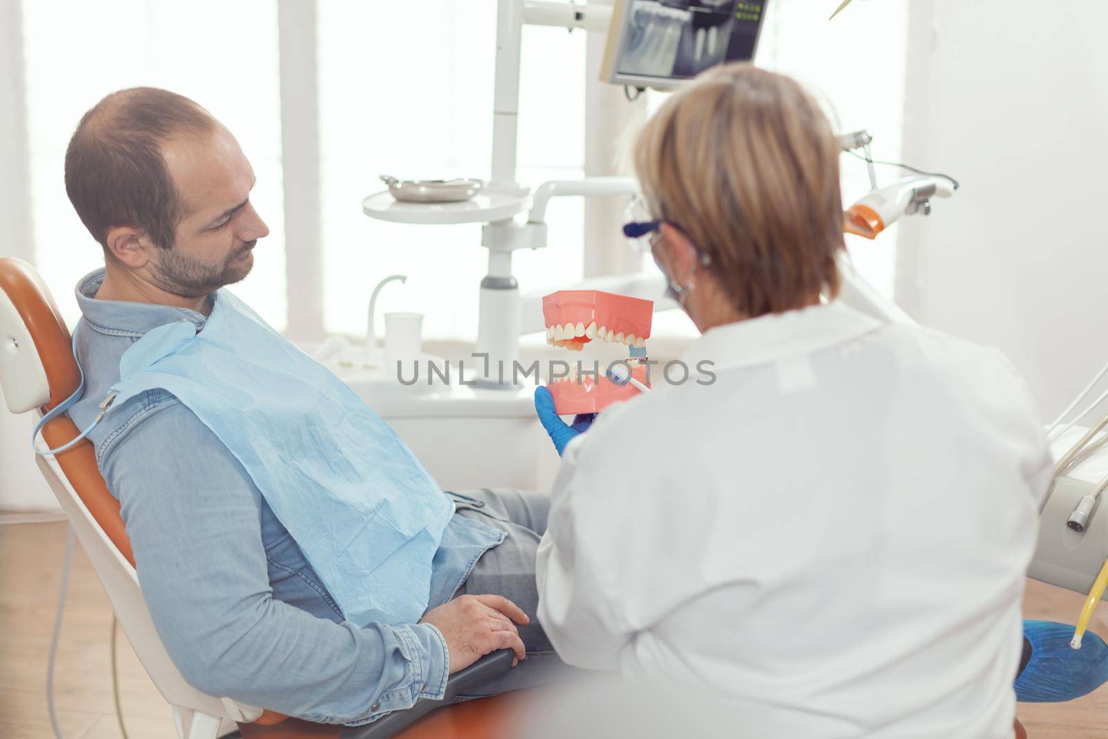 Stomatologist holding sanitary model of the mandible talking with sick man by DCStudio