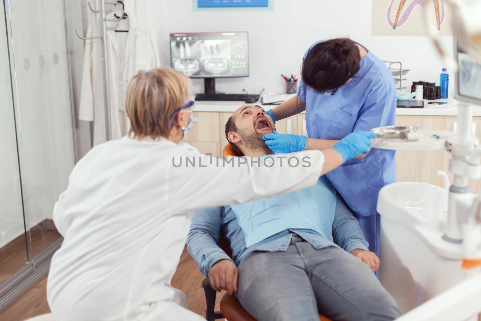 Sick man sitting on dental chair while medical nurse looking into mouth by DCStudio