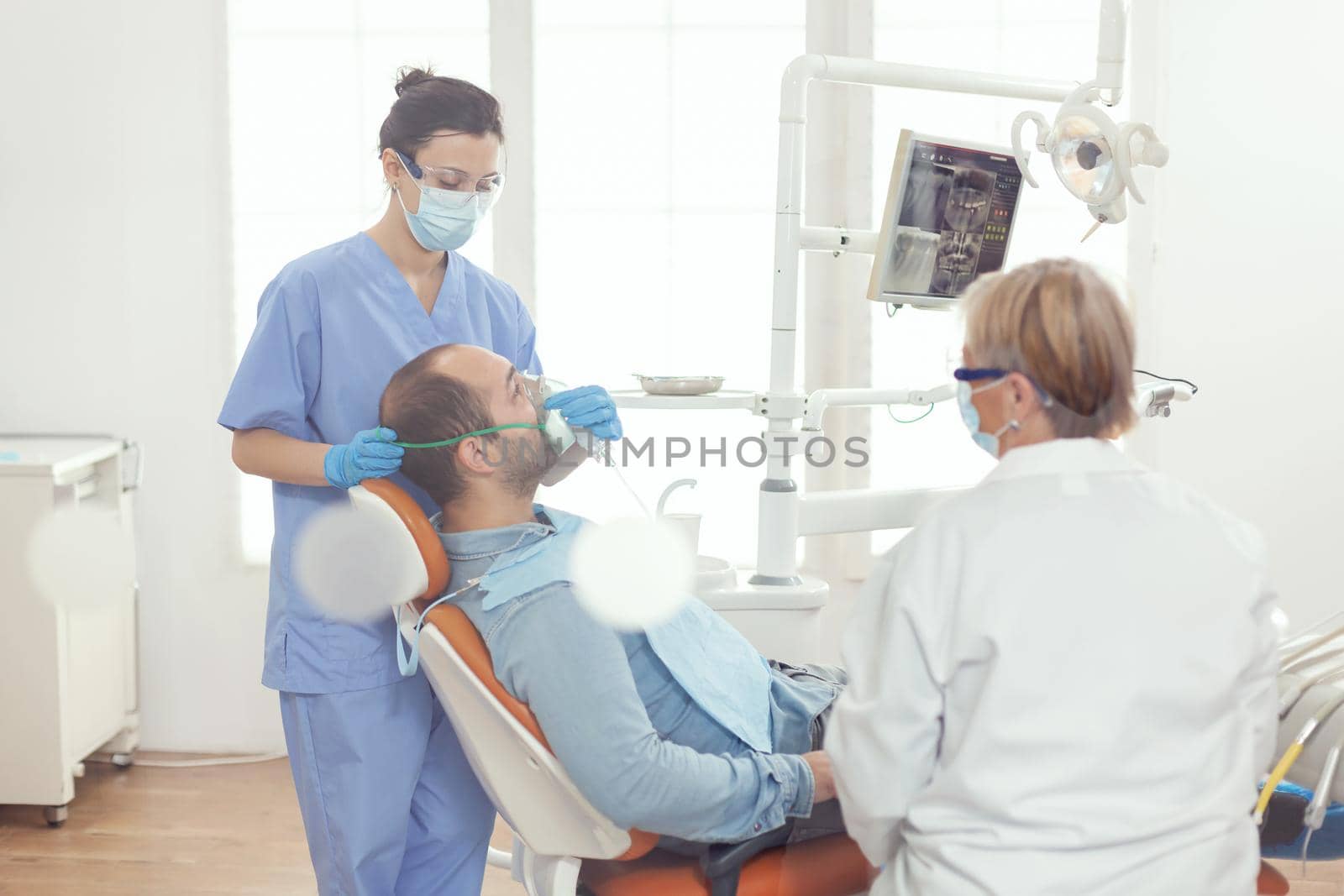 Medical assistant putting oxigen mask examining sick man patient for dentistry surgery by DCStudio