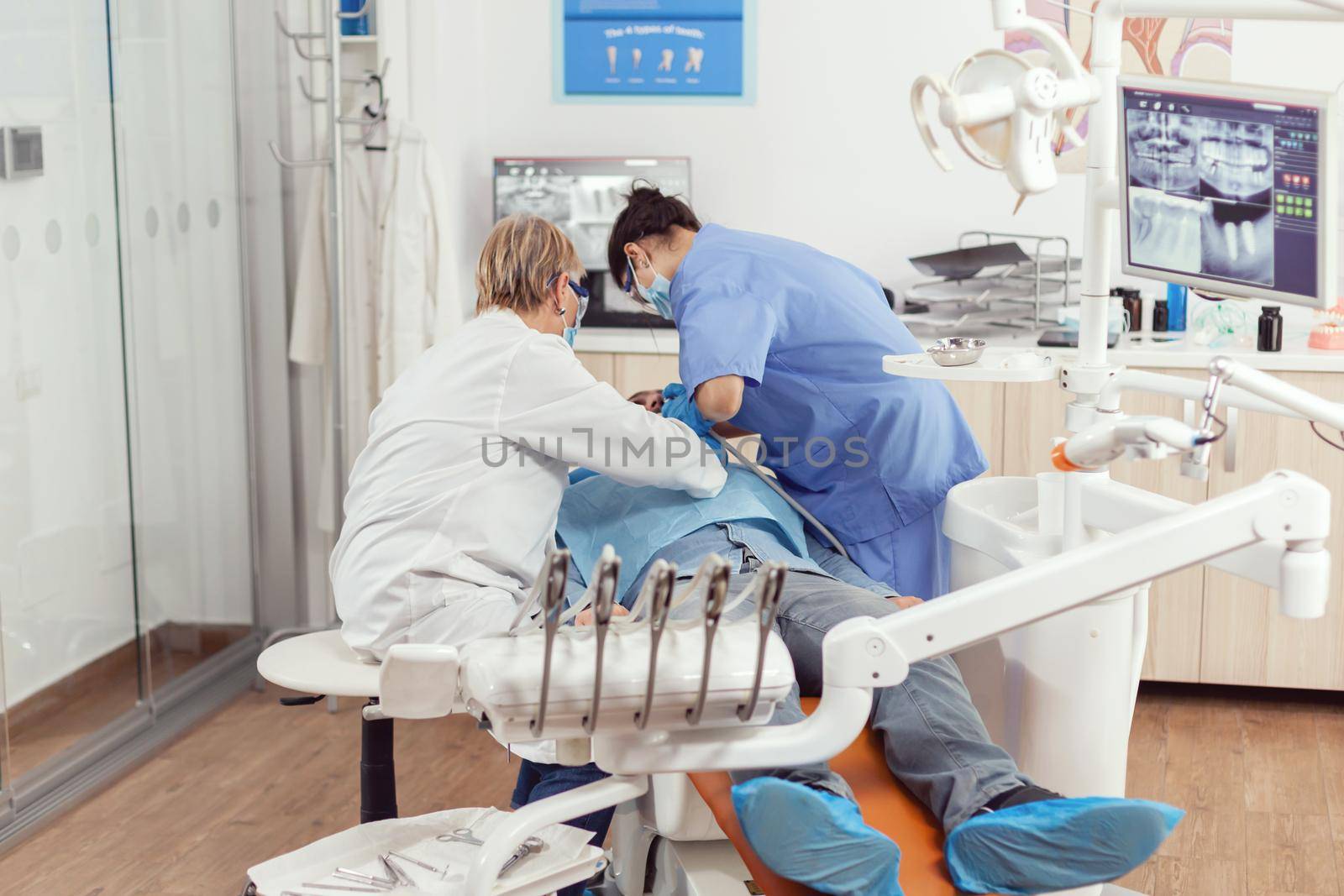 Senior dentist woman performing surgery putting implant into sick man mouth in dental clinic. Dentistry doctor with protection mask treating teeth of patient sitting on chair during consultation