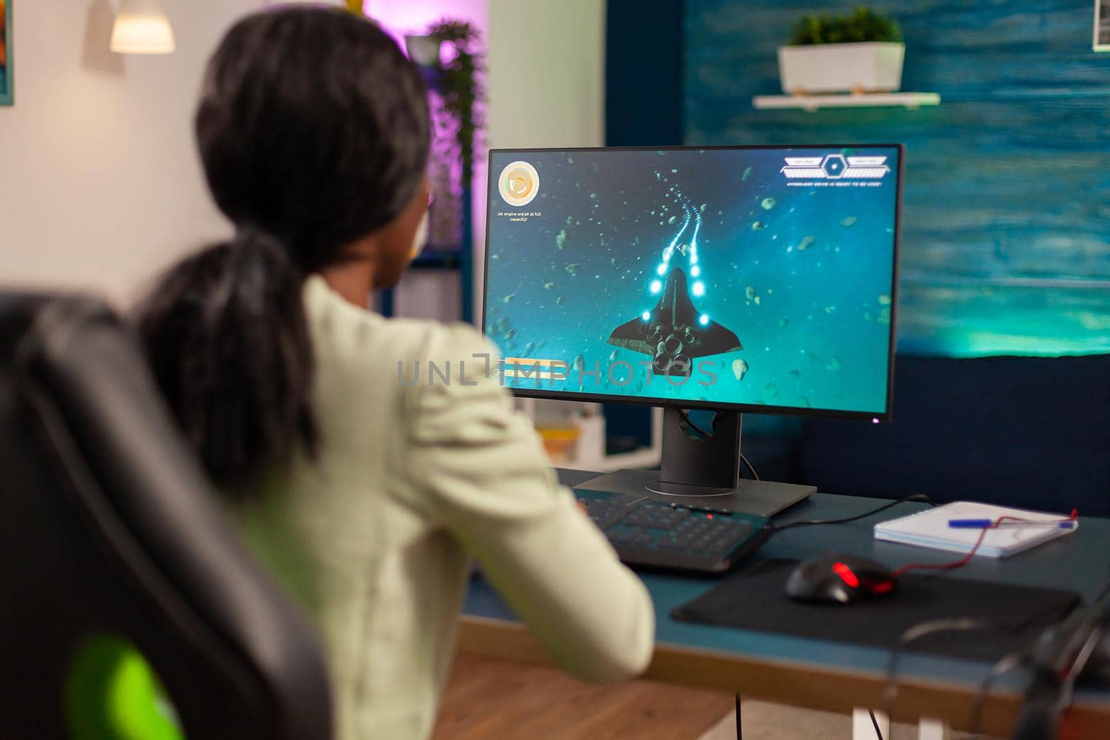 Pro african gamer playing space shooter with wireless joystick at night. Competitive cyber player woman performing videogame tournament use professional joystick.