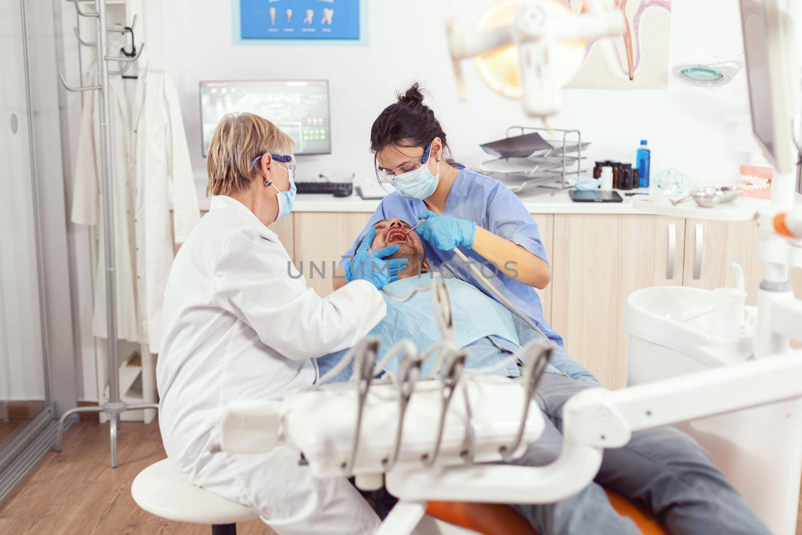 Sick patient sitting on stomatology chair while medical nurse looking into mouth analyzing teeth health during stomatology examination. Senior dentist woman waiting for stomatological procedure