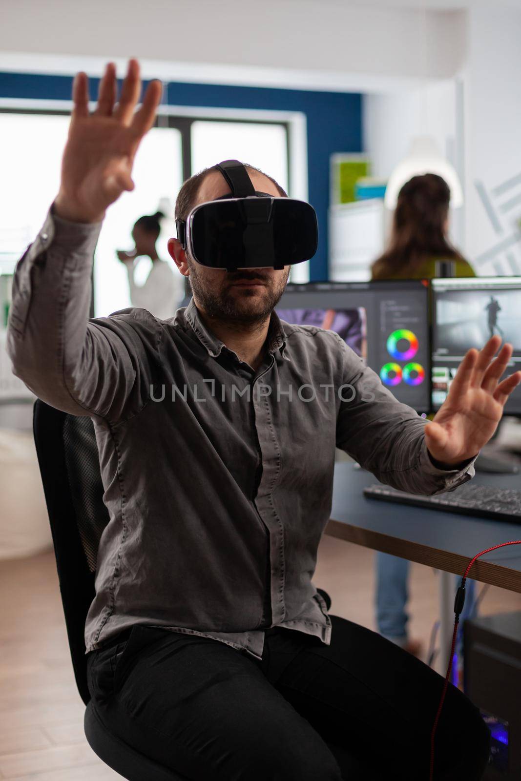 Videographer wearing VR headset and gesturing editing project in post production software sitting in studio office. Man video maker employee processing film montage in digital multimedia company