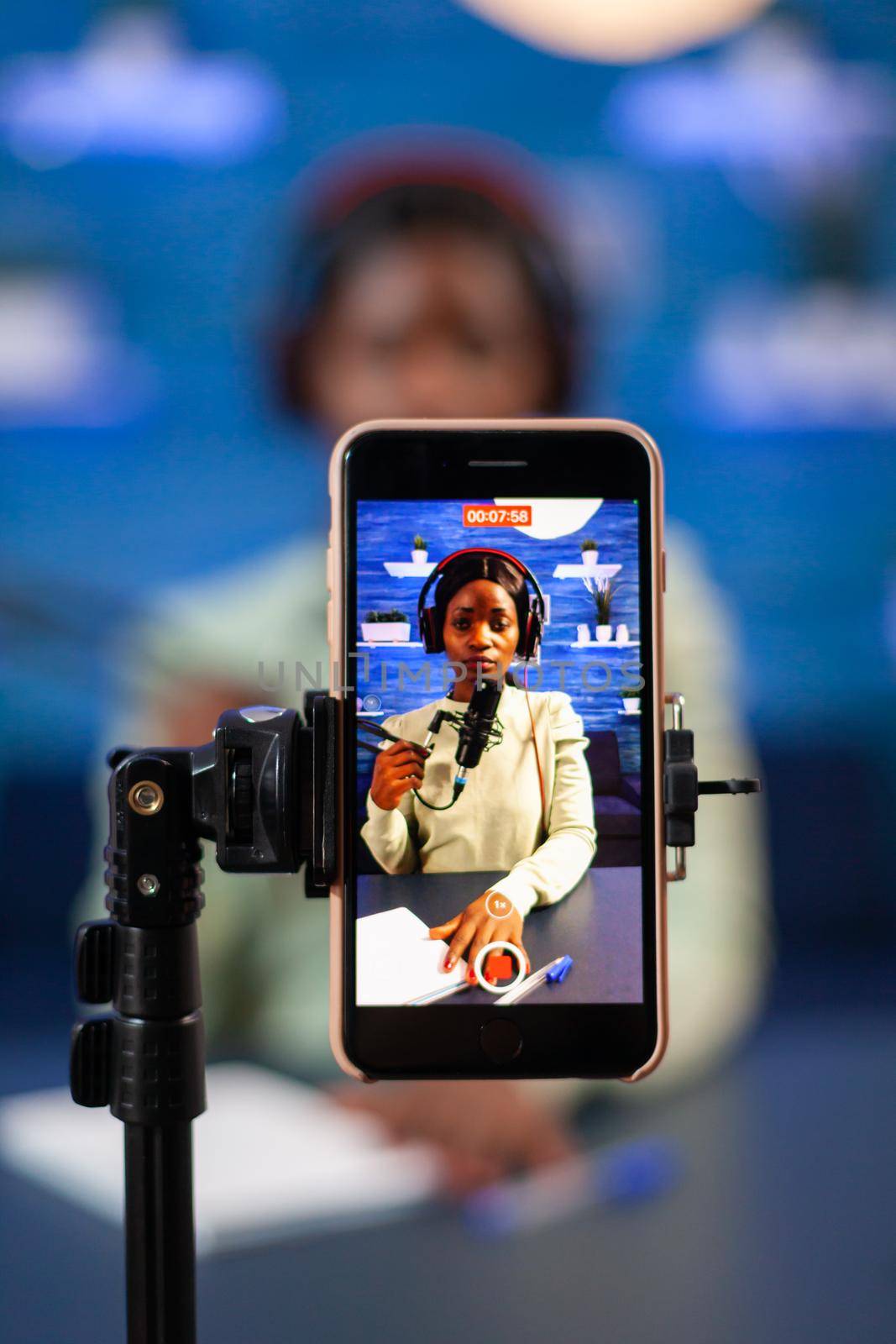 Close up of smartphone recording vlog of african influencer in home studio. Speaking during livestreaming, blogger discussing in podcast wearing headphones.