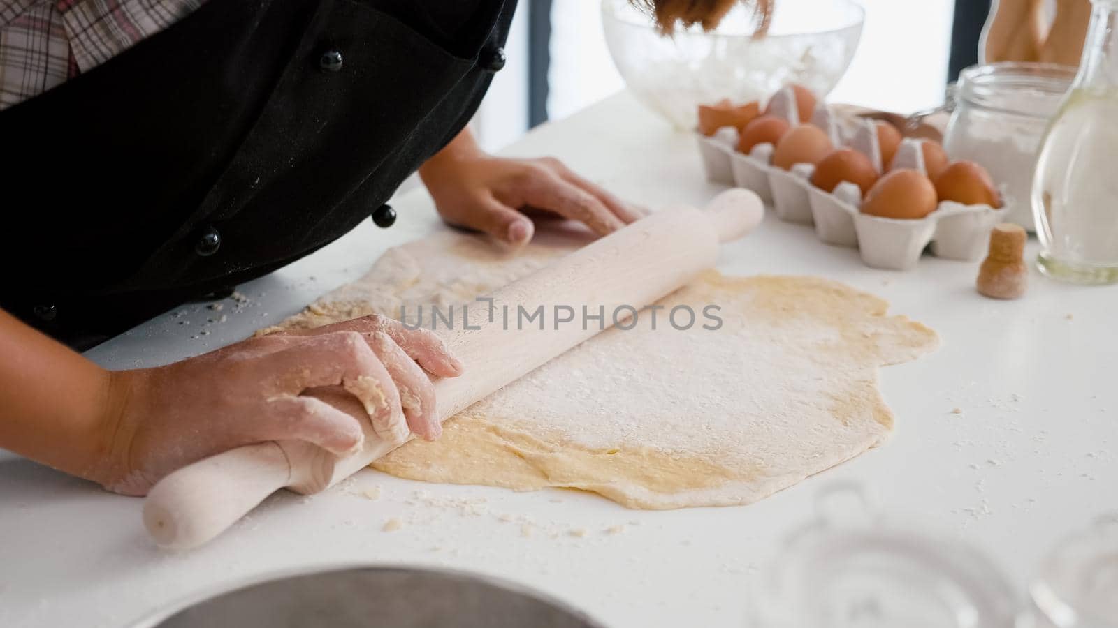 Close up of children hand preparing homemade gingerbread making cookies dough using traditional rolling pin in culinary kitchen. Happy family enjoying cooking dessert during christmas holiday