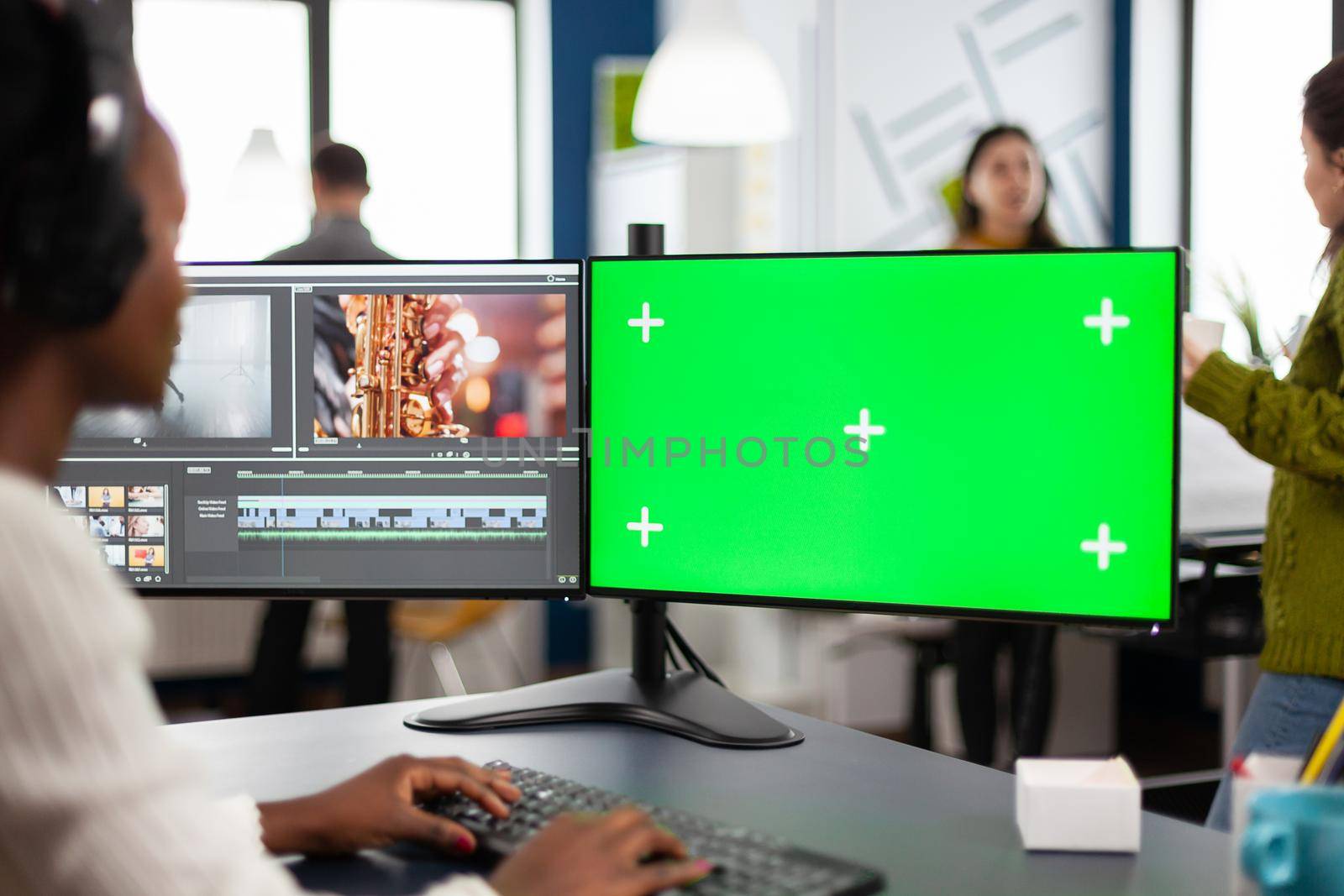 African video editor with headset editing footage using pc with greenscreen by DCStudio