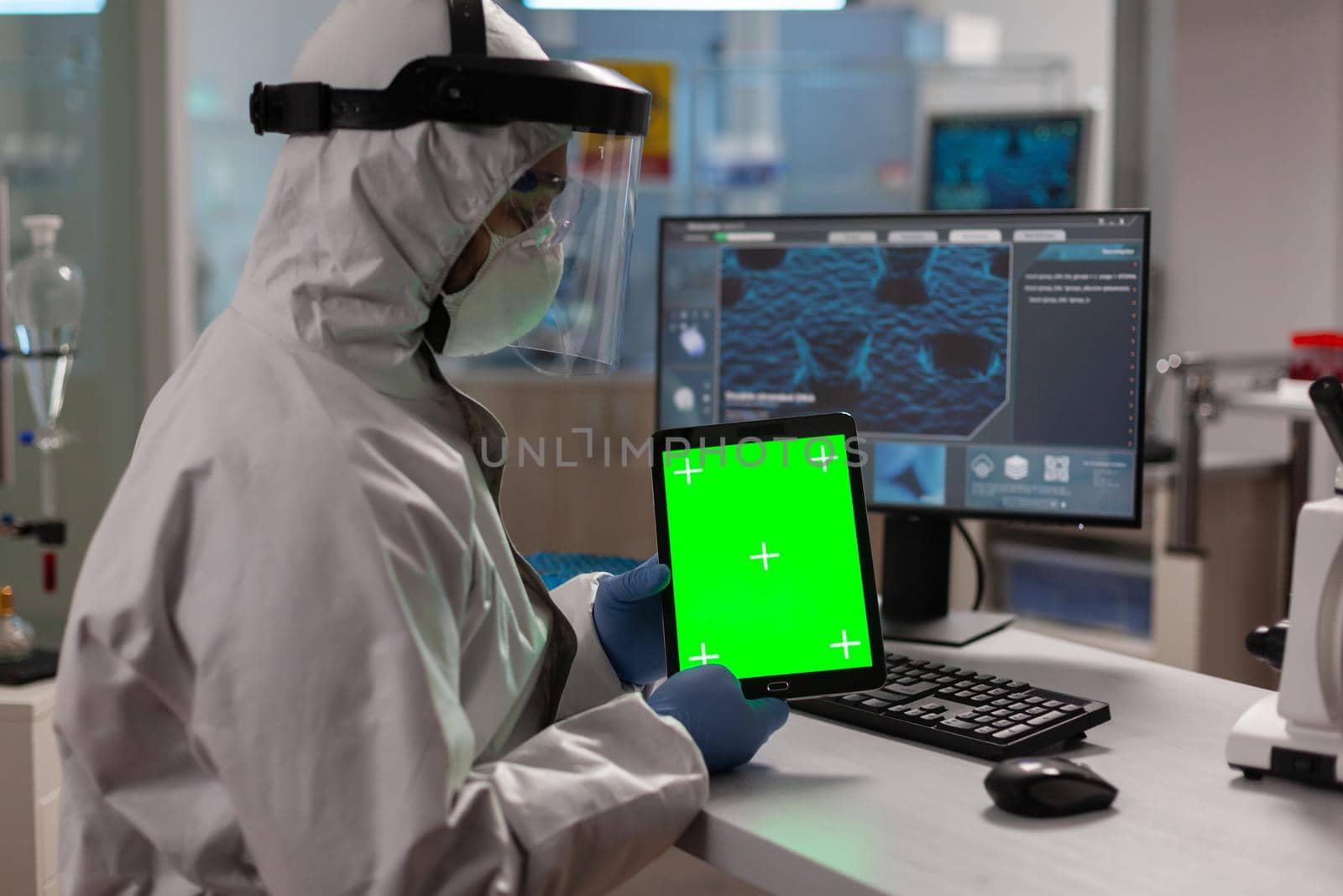 Doctor with coverall working on tablet with green screen in modern equipped lab.Team of microbiologists doing vaccine research writing on device with chroma key, isolated display.