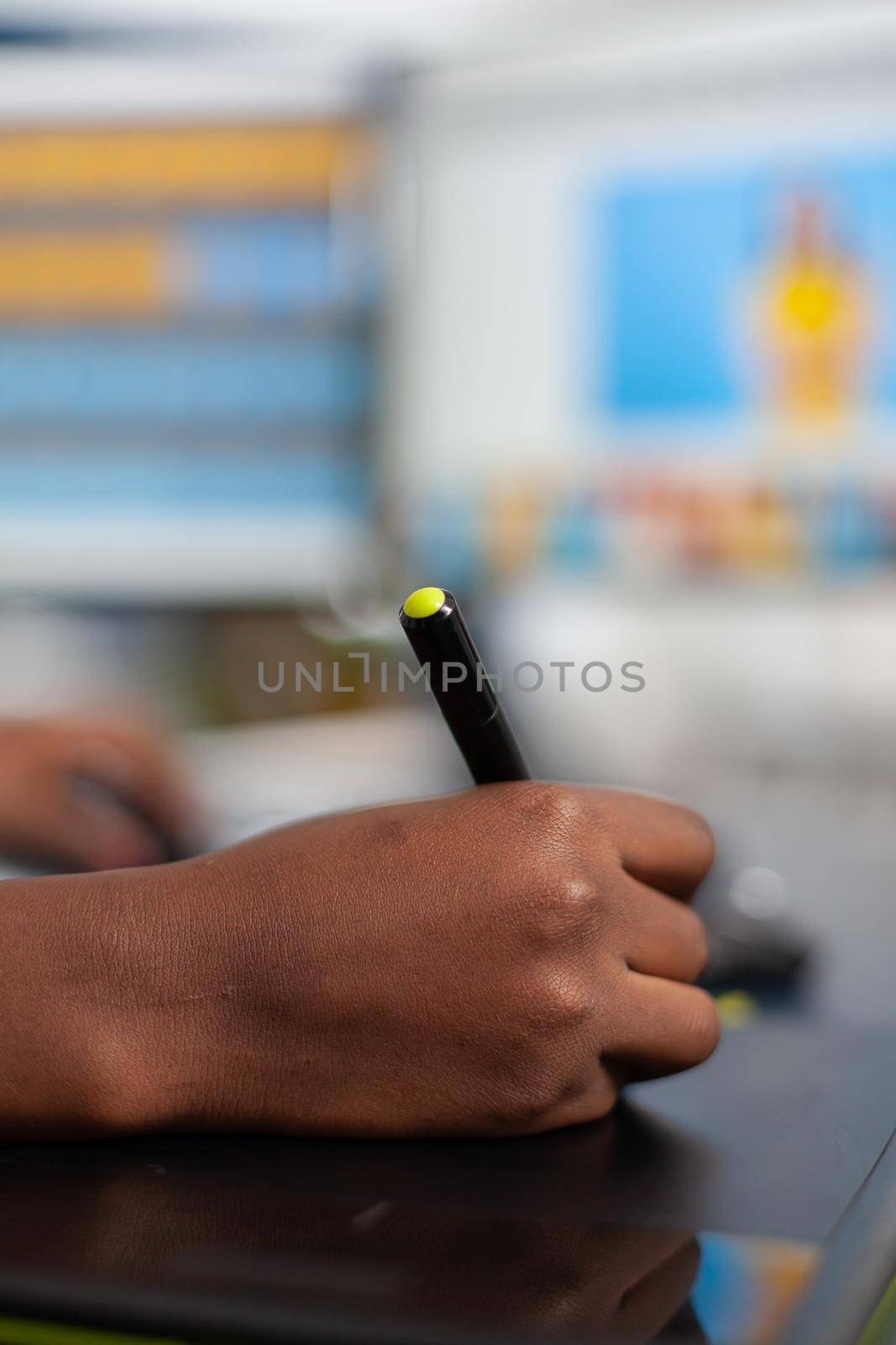 Close up of african photo retoucher holding stylus pen editing customer photo using computer with two displays. Black woman editor retouching assets drawing on graphic tablet in creative agency office