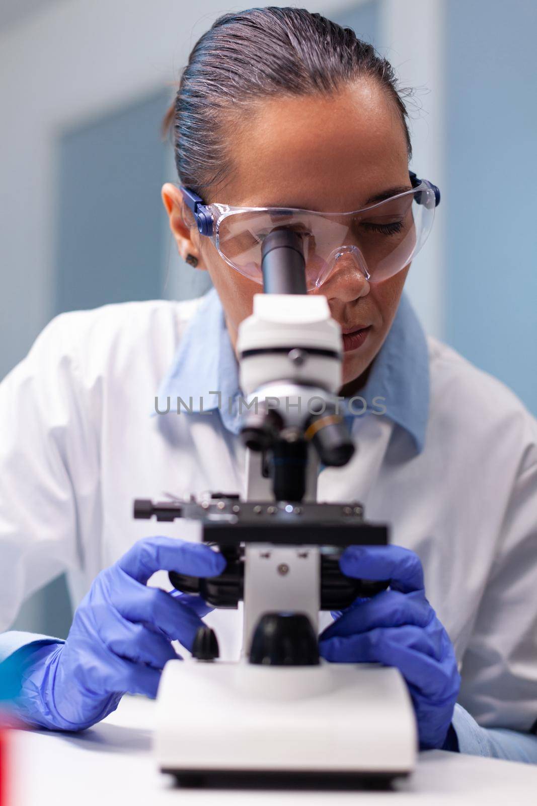 Scientist woman doctor looking at coronavirus genetics test using medical microscope working at bacteriology experiment in hospital laboratory. Researcher microbiologist discovering medicine vaccine