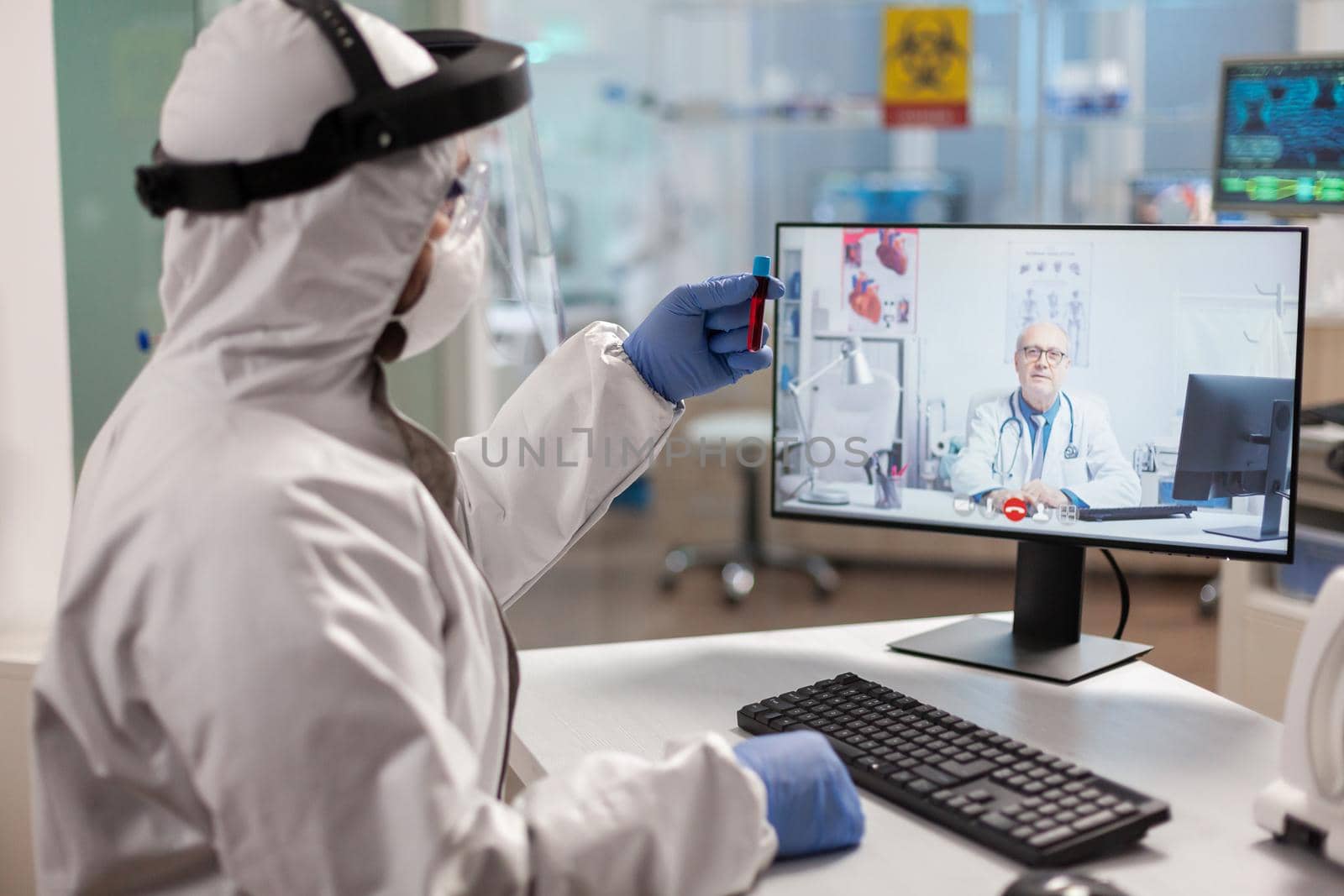 Senior man doctor offering medical online advices to chemist in ppe suit by DCStudio