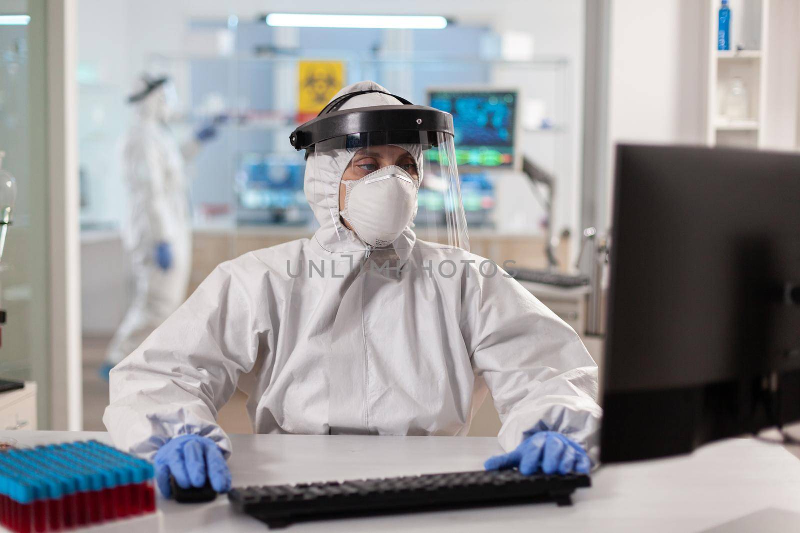 Scientist dressed in ppe suit working on computer for virus vaccine. Doctor working with various bacteria, tissue, pharmaceutical research for antibiotics against covid19.