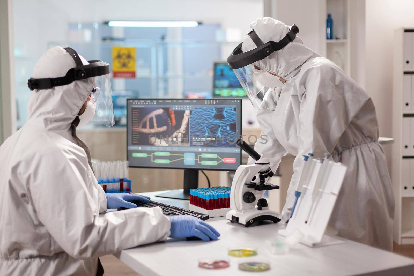 Scientists in protection suits analysing dna sample infected with virus. by DCStudio