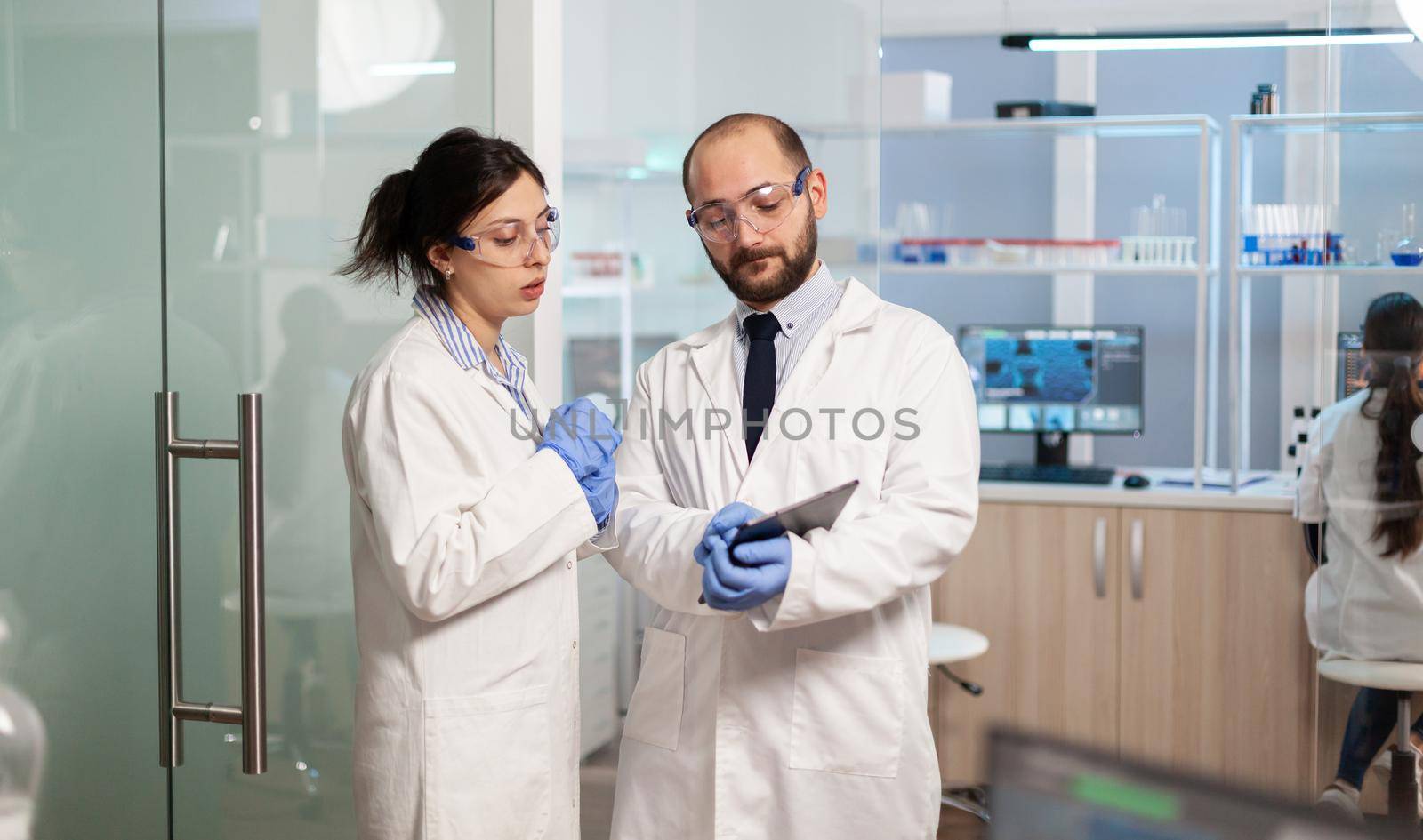 Team of medical scientists conducting vaccine development with help of high tech technology, doctor holding tablet analysing new informations. Examining virus evolution using devices researching diagnosis.