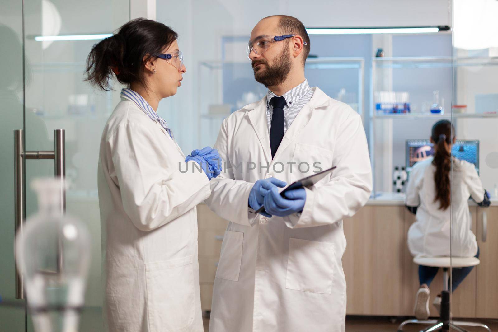 Scientists coworkers using digital tablet working in medical research laboratory, analysing biochemicals samples, talking. Scientific lab for medicine, microbiology development with advanced equipment.